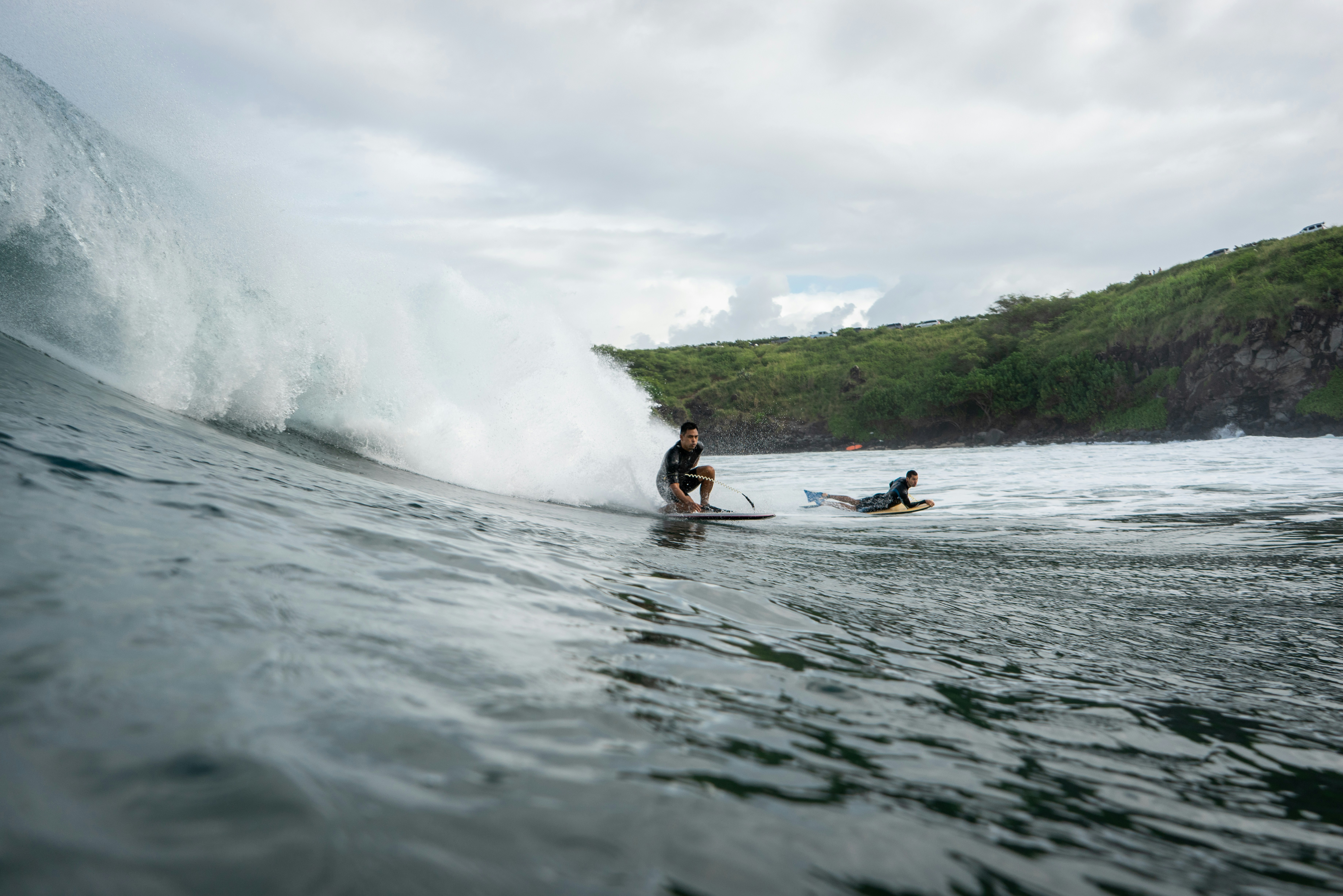 Surfers riding waves near a lush green coastline.
