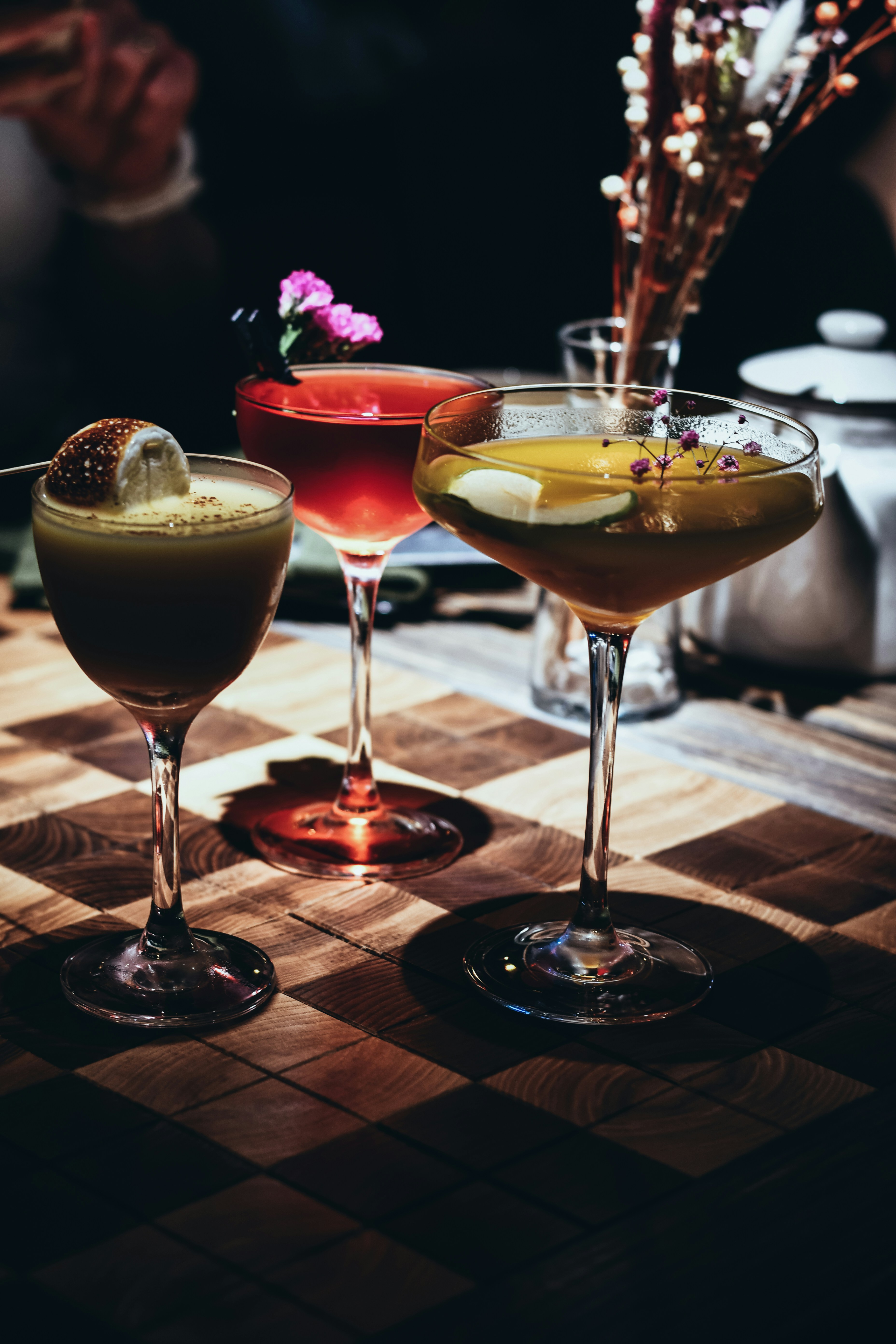 Three colorful cocktails garnished with fruit and flowers