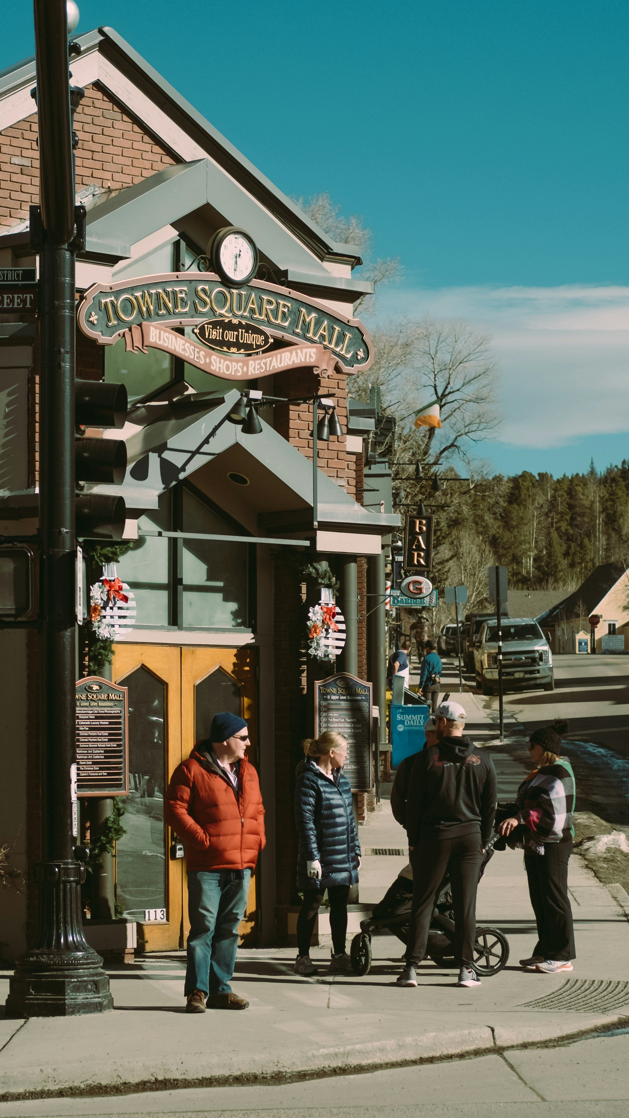 People standing on a sunny street corner near a mall.