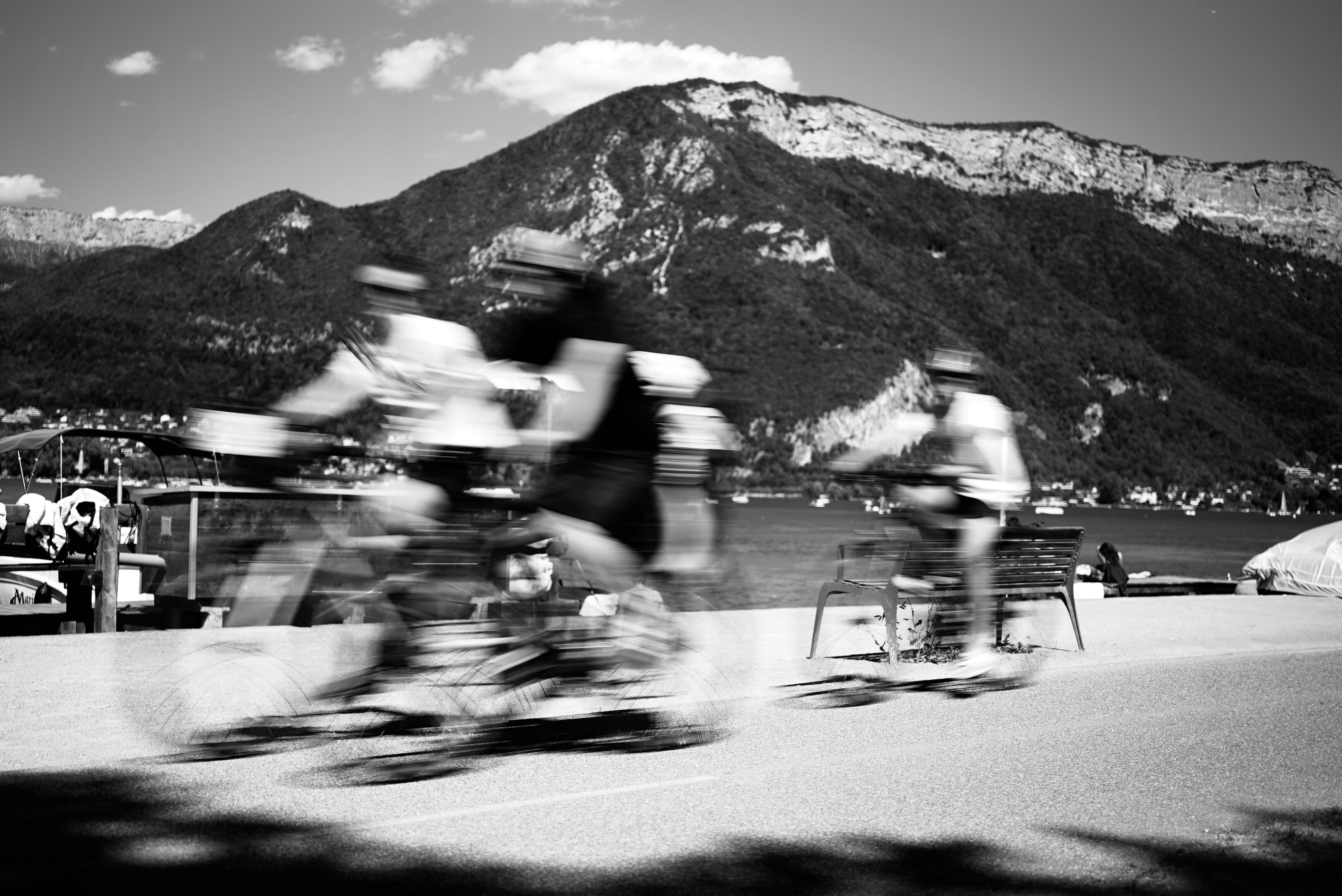 Cyclists race past a lake with mountains behind.