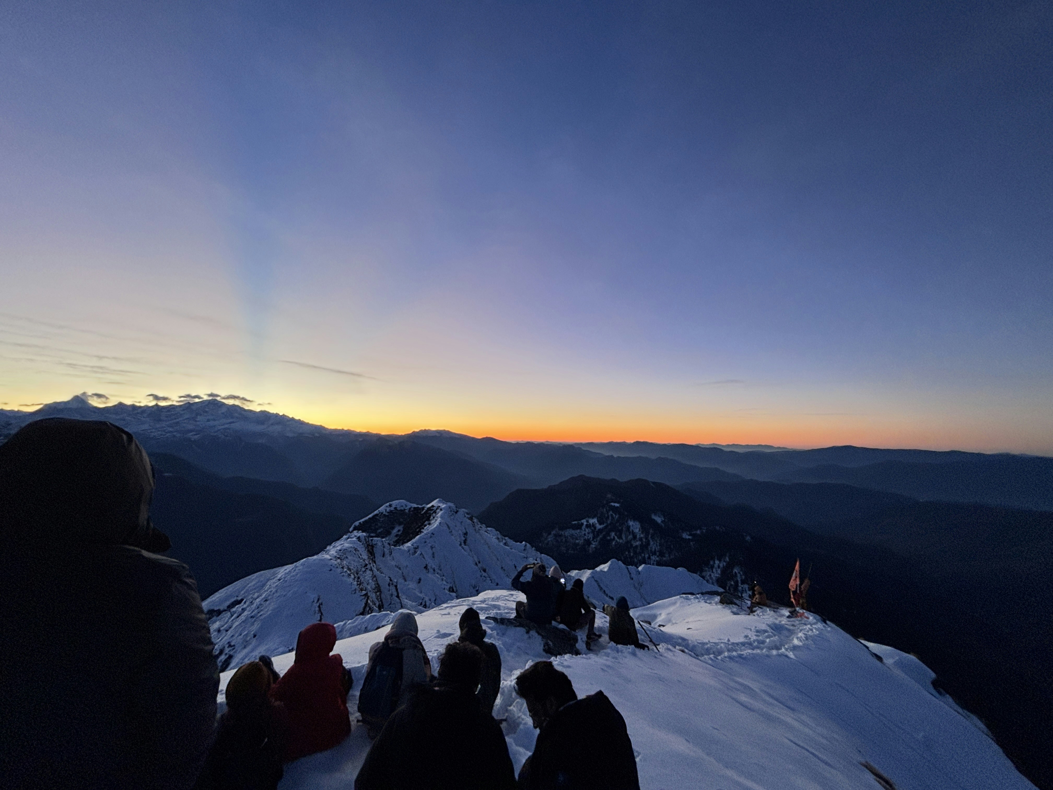 People watch the sunrise from a snowy mountain peak.