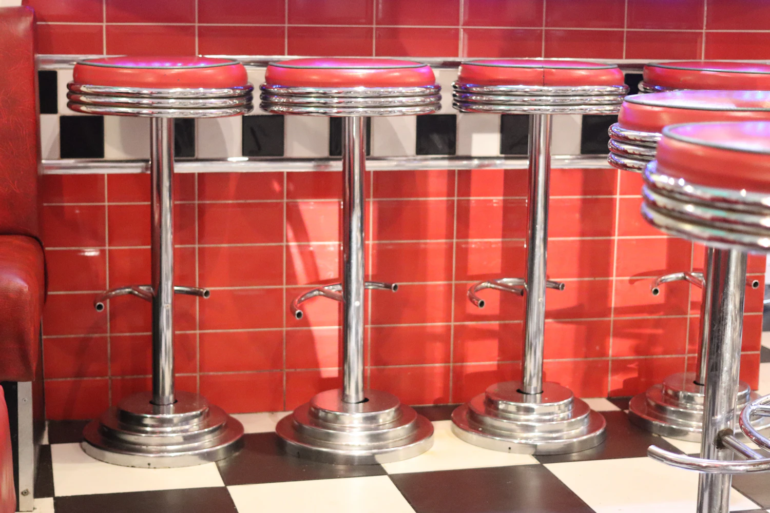 A row of chrome and red stools along a tiled counter