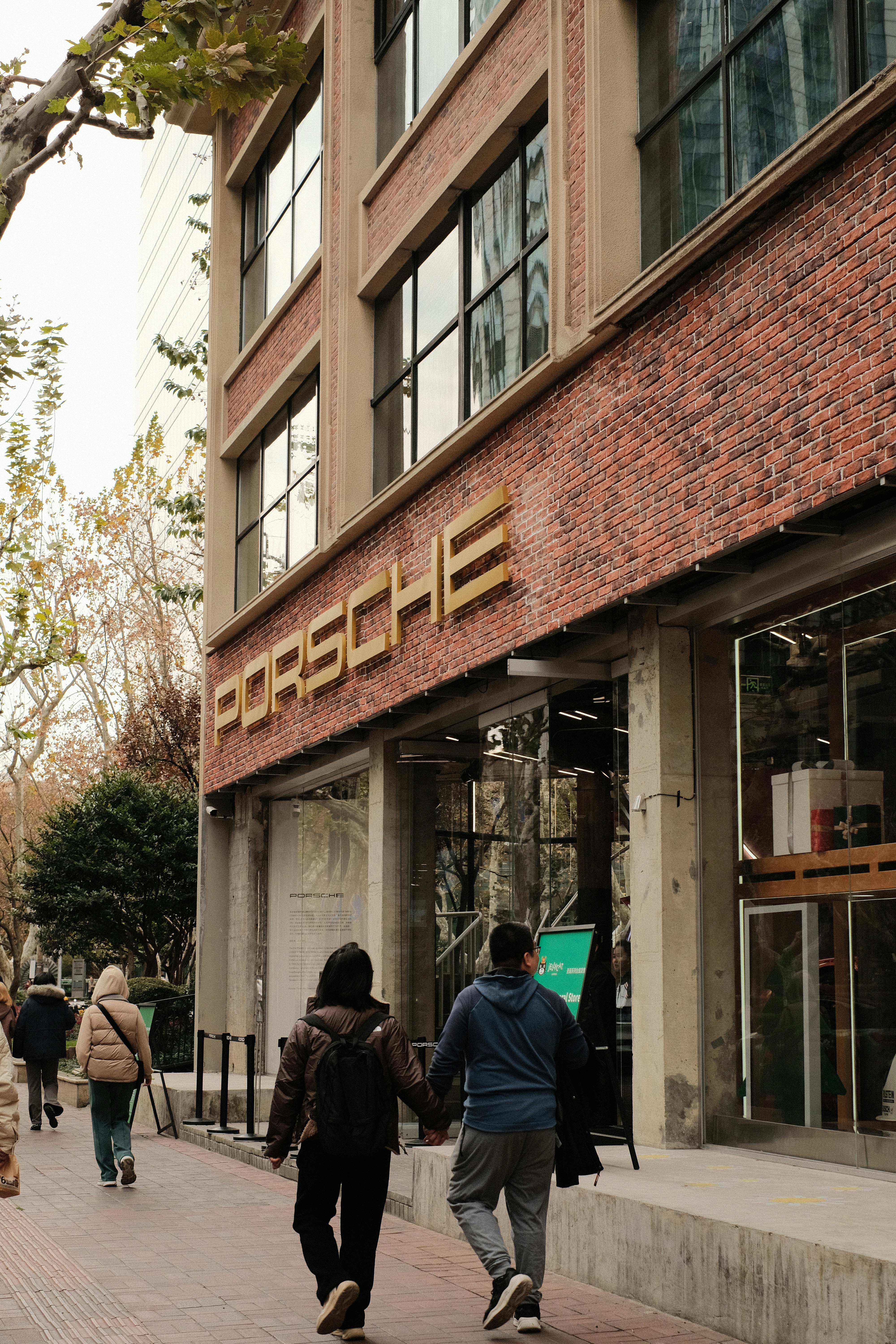 Couple walking hand-in-hand outside porsche building.