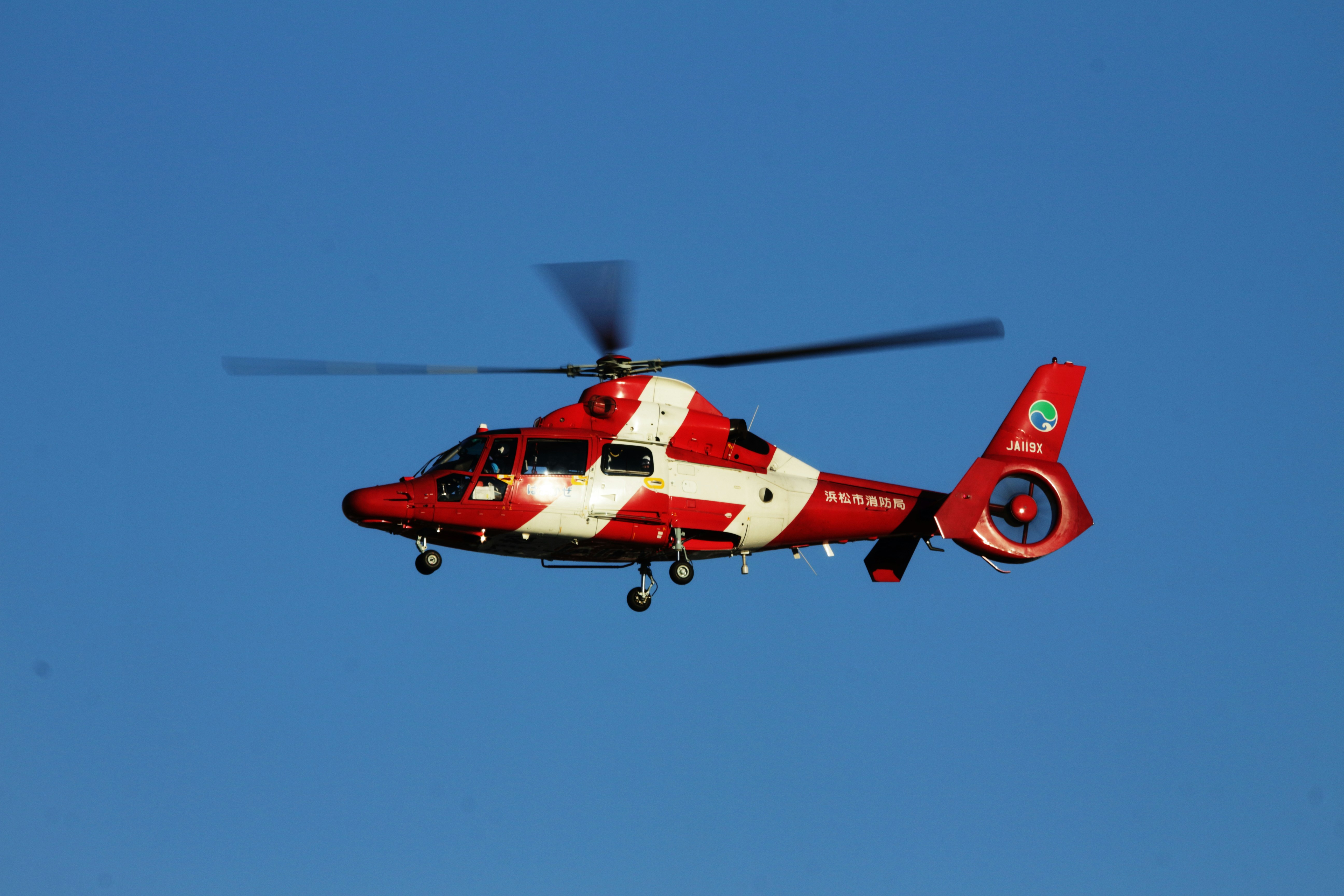 Red and white helicopter flying against a blue sky.