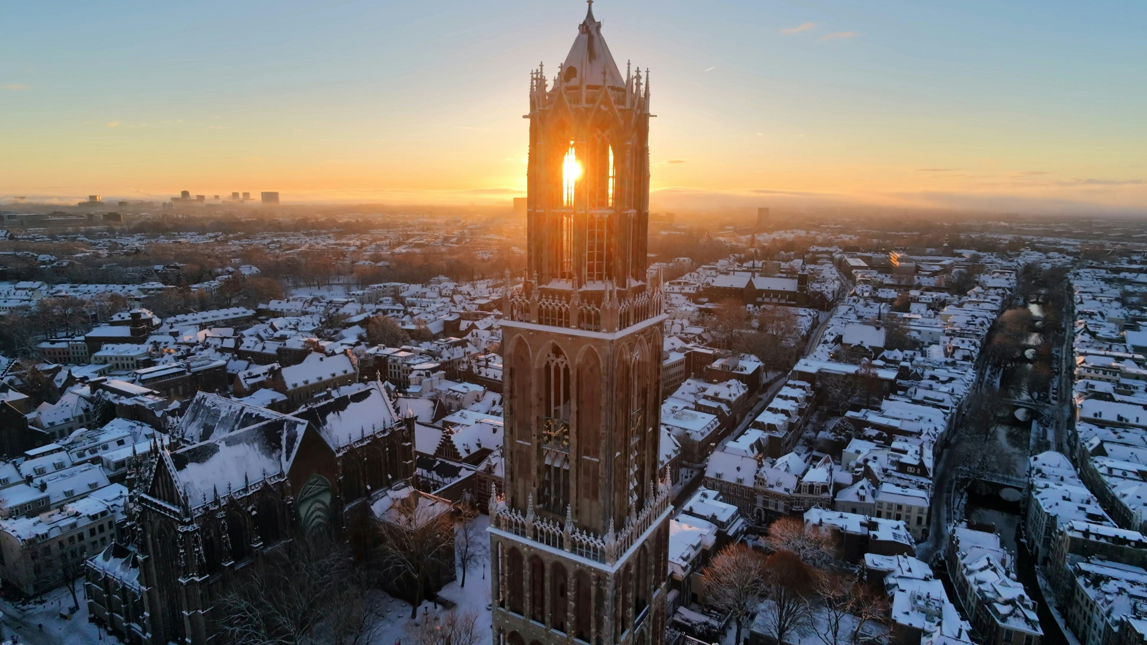 Sunrise behind a tall church tower in a snowy city.