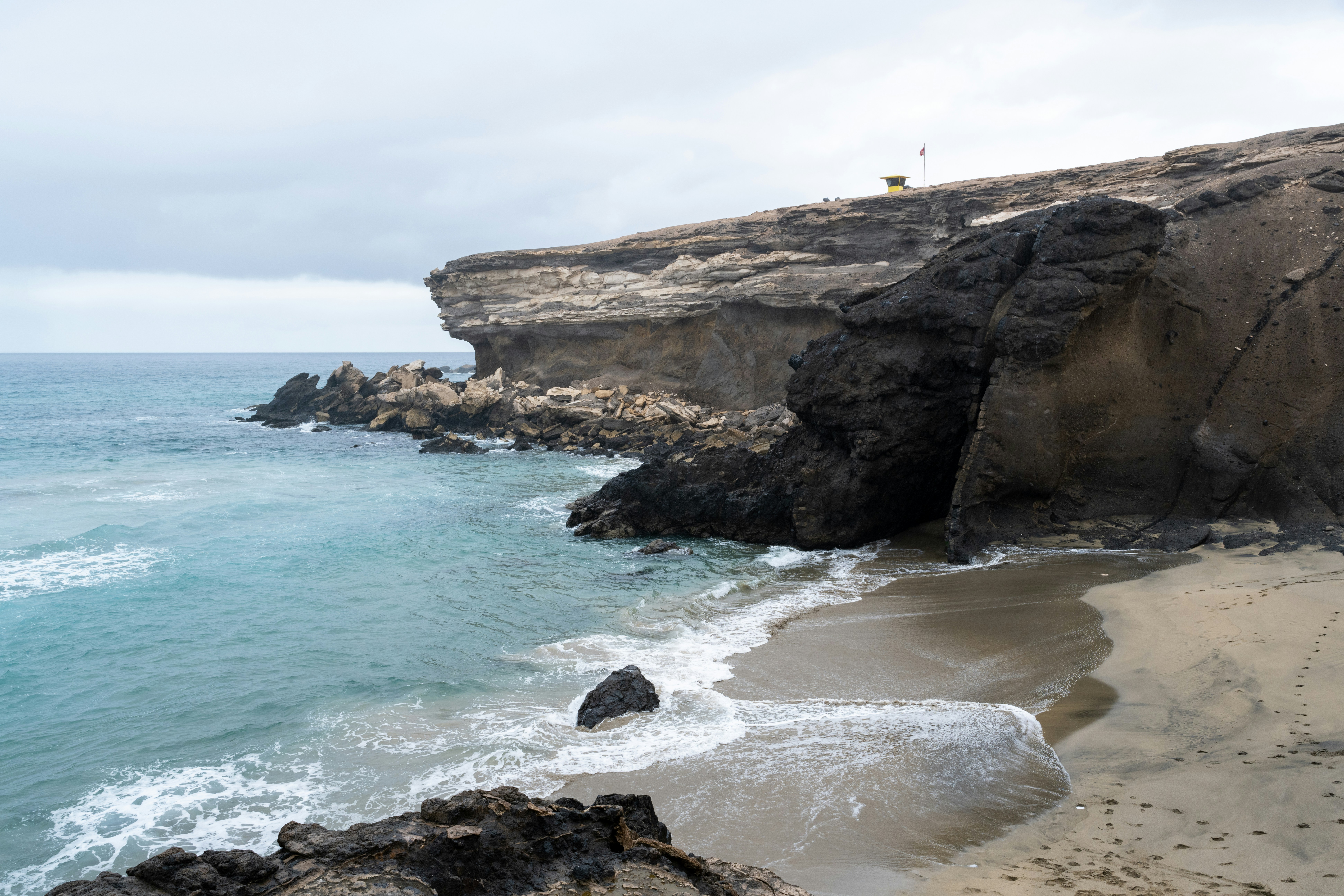 Zerklüftete Klippen treffen auf das Meer an einem Sandstrand.