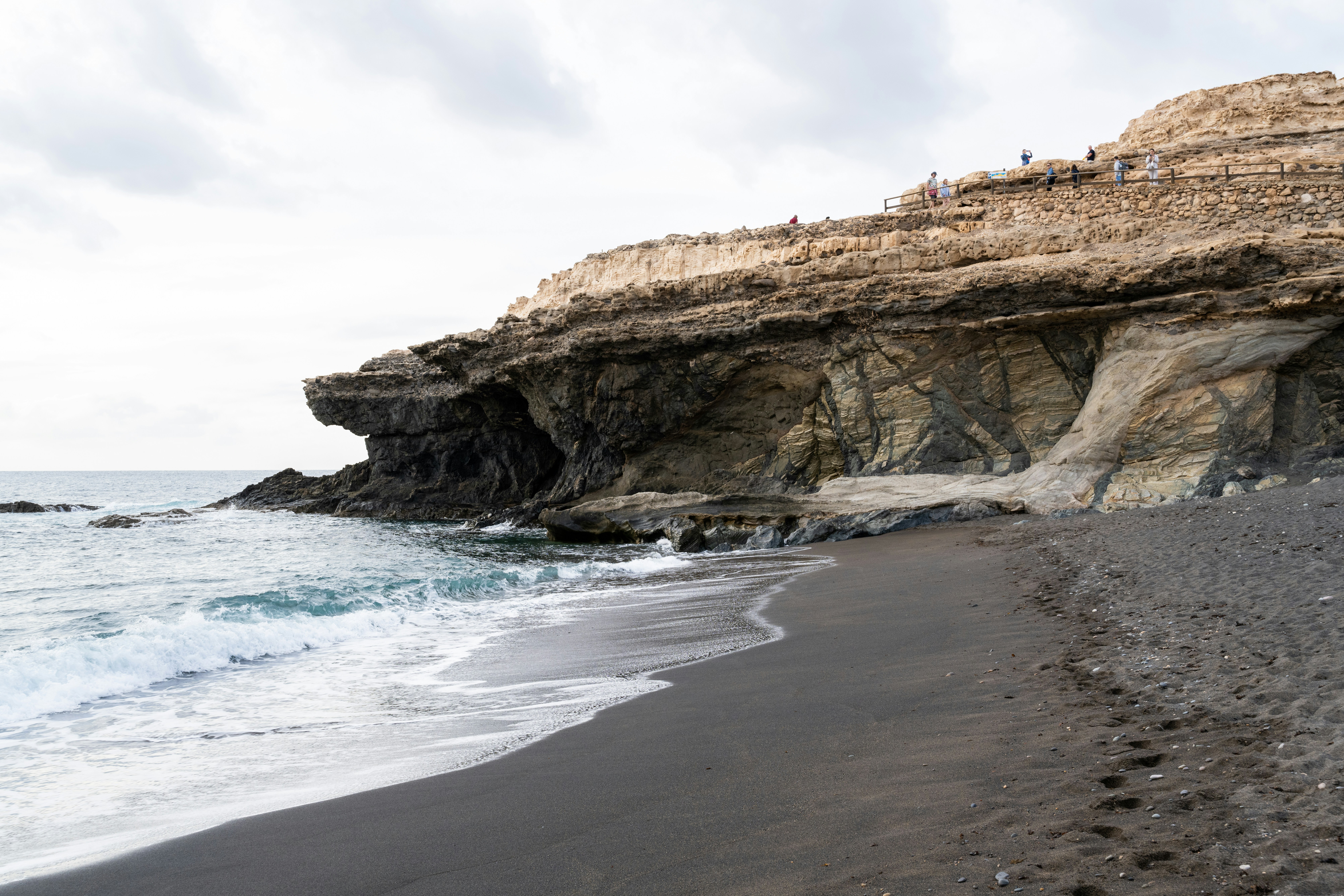 Schwarzer Sandstrand mit felsigen Klippen und Meereswellen