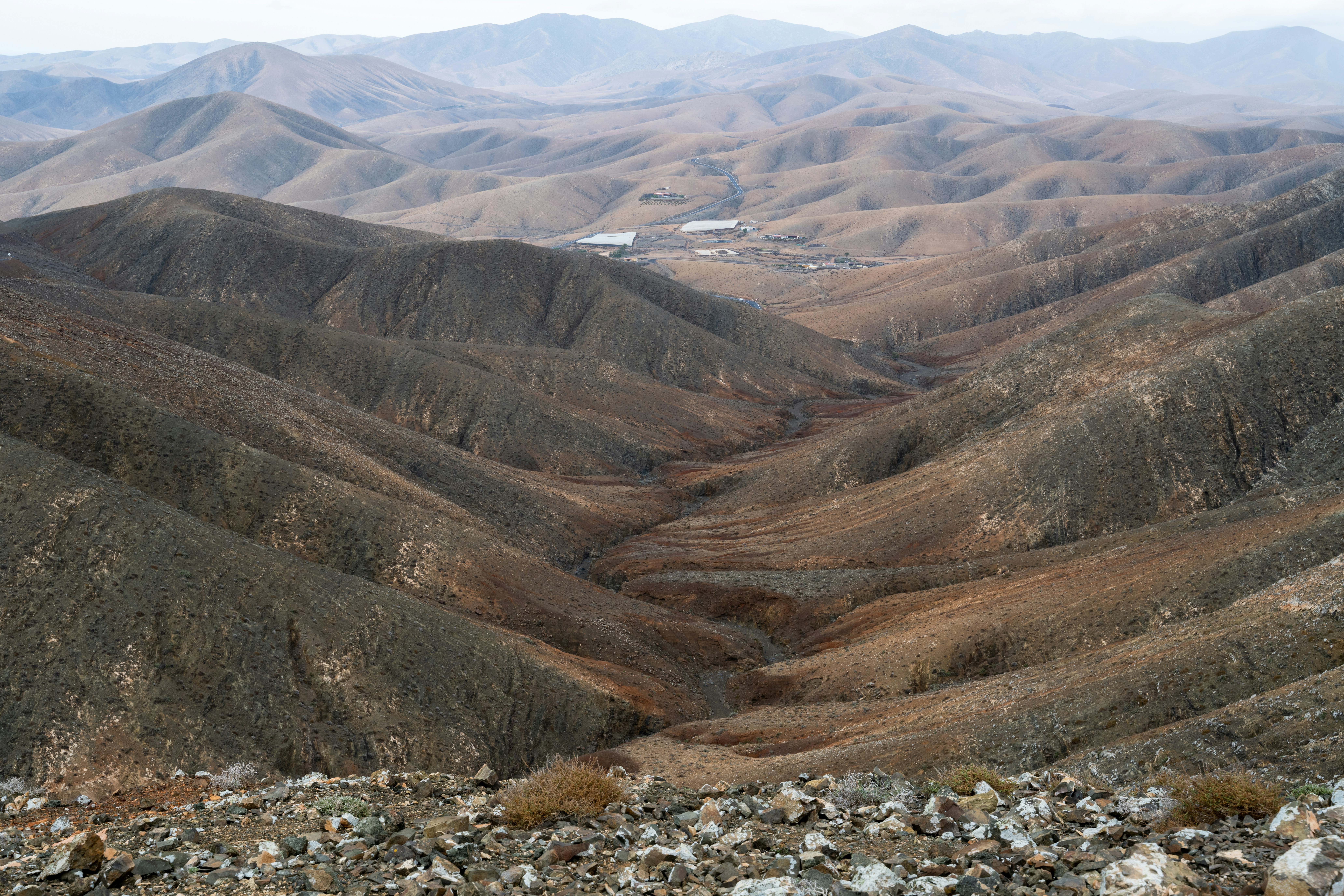 Trockenes Bergtal mit trockenem Gestrüpp und entfernten Gebäuden