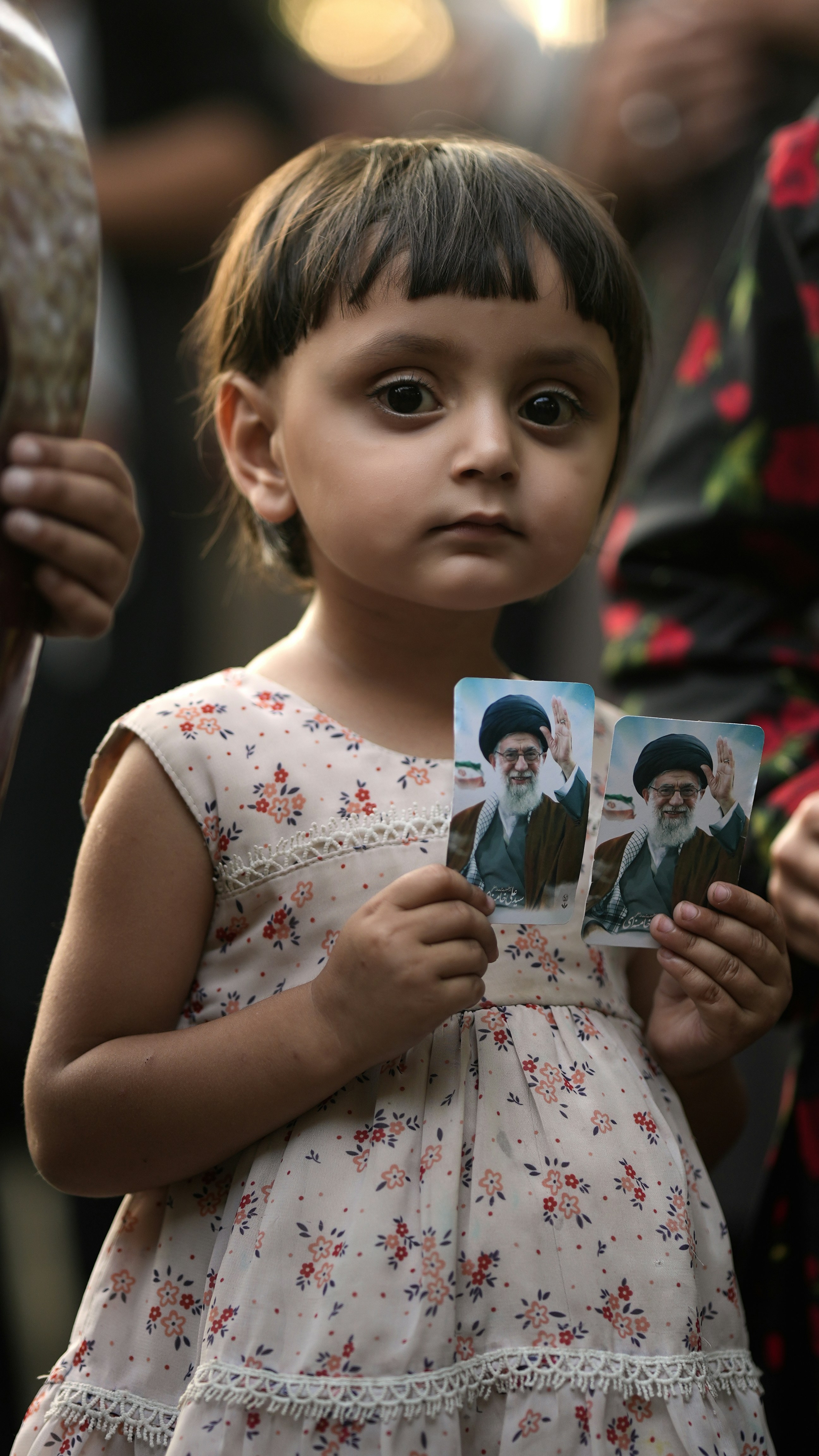 Young girl holds two portraits of a man.
