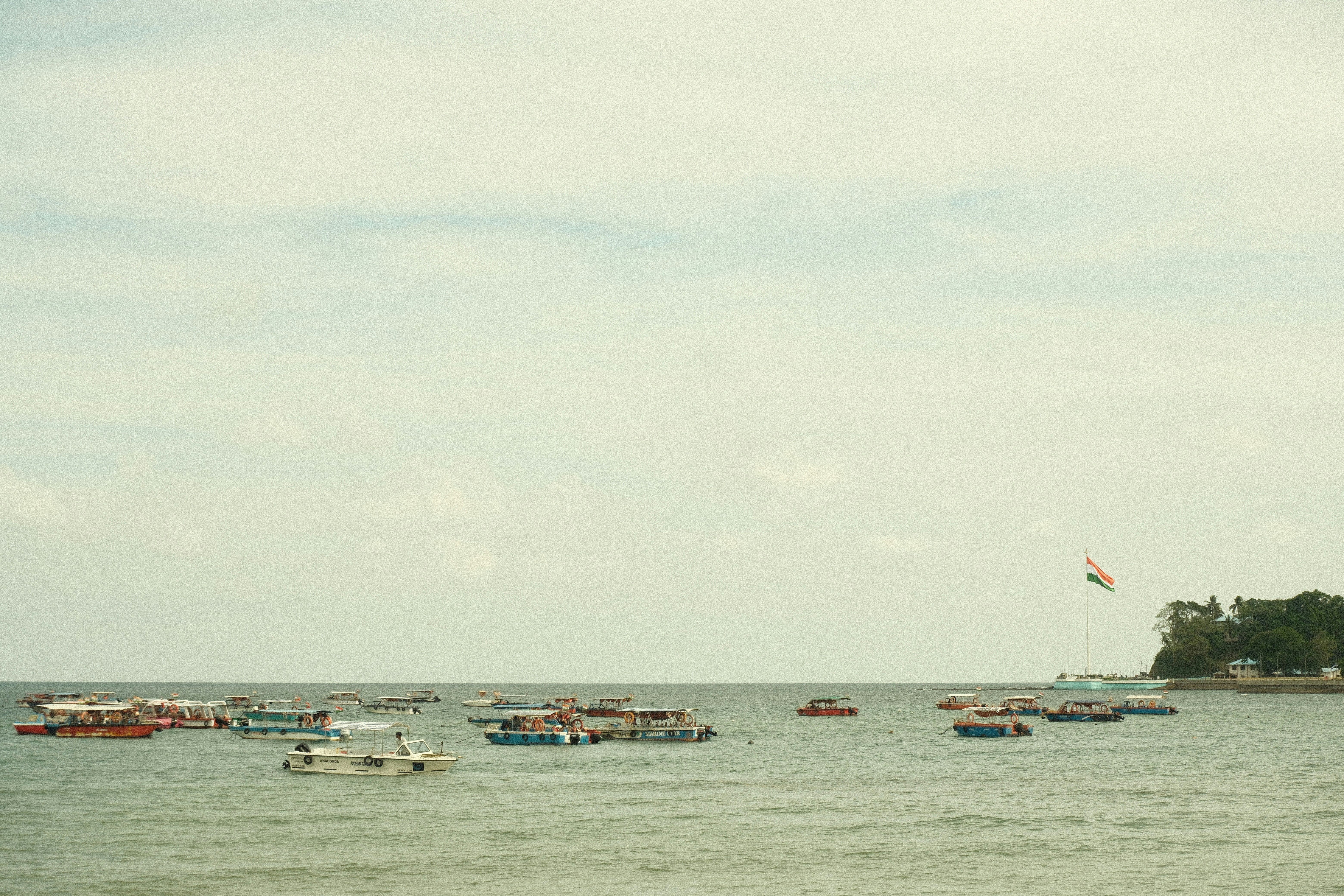Many boats float on the calm ocean near land.