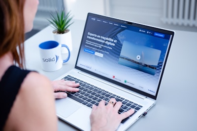 Woman typing on laptop with website on screen.