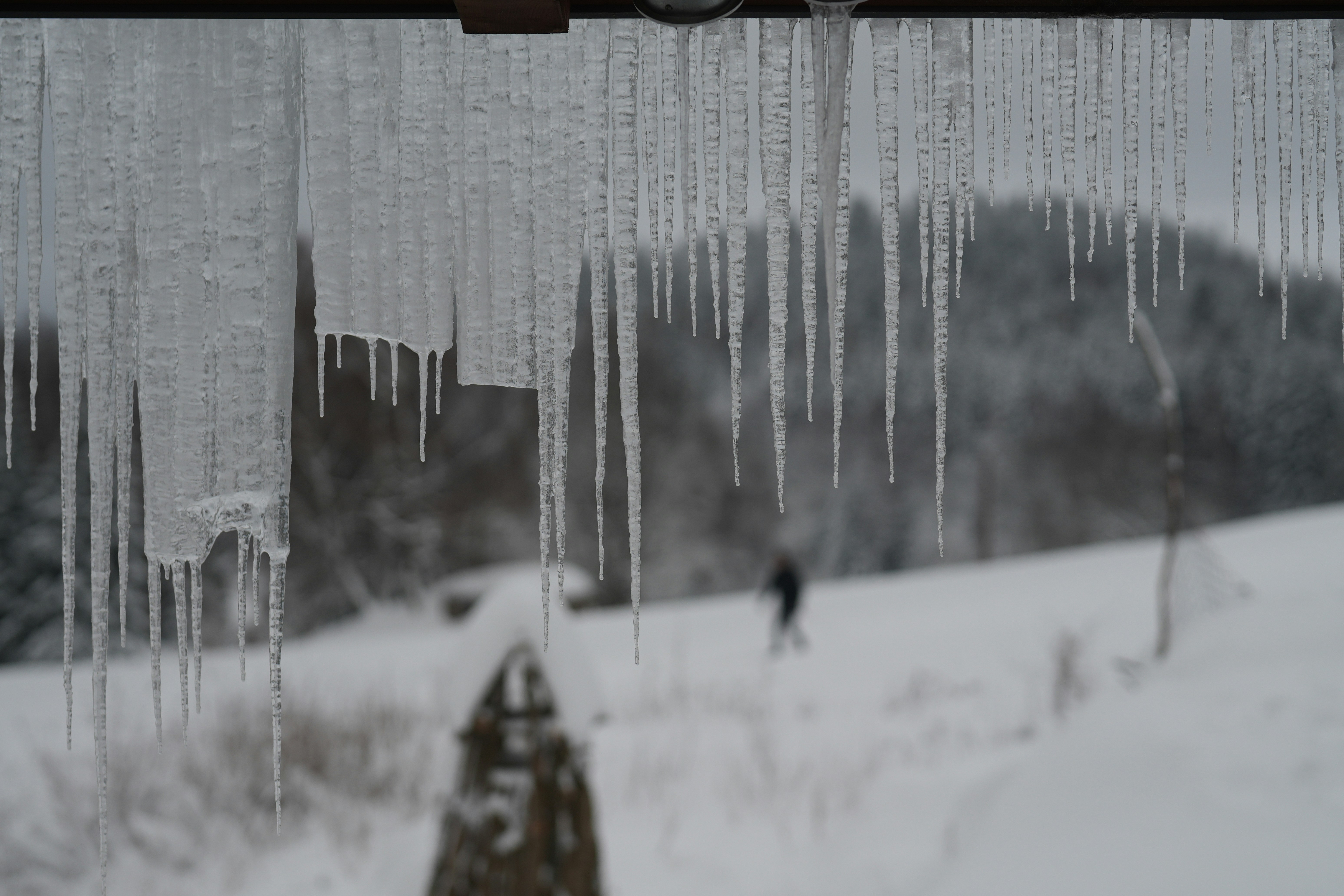 Icicles hang above a snowy landscape with a person.
