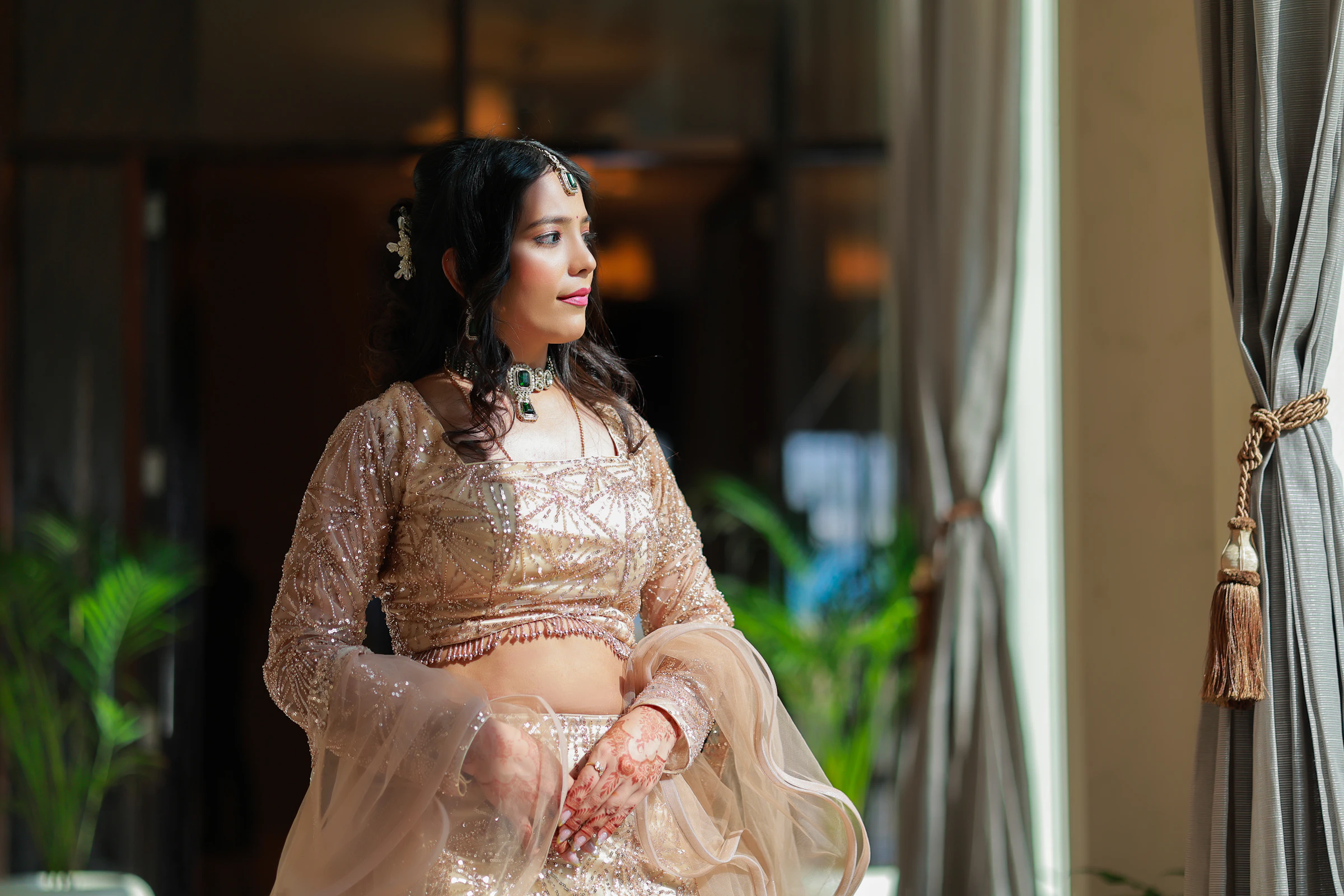 A young woman in an ivory embroidered lehenga by a window