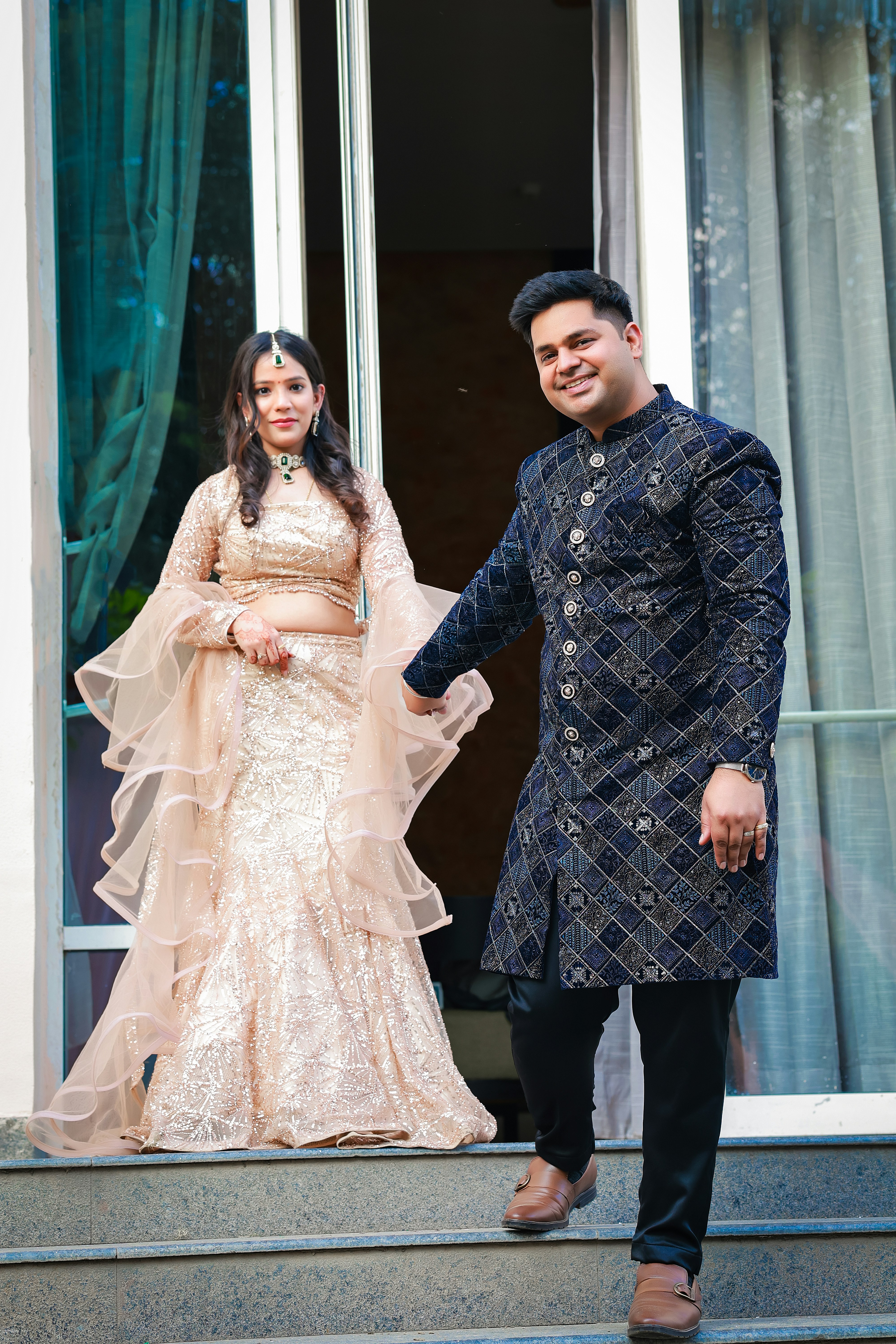 A smiling couple in traditional indian attire walks downstairs.