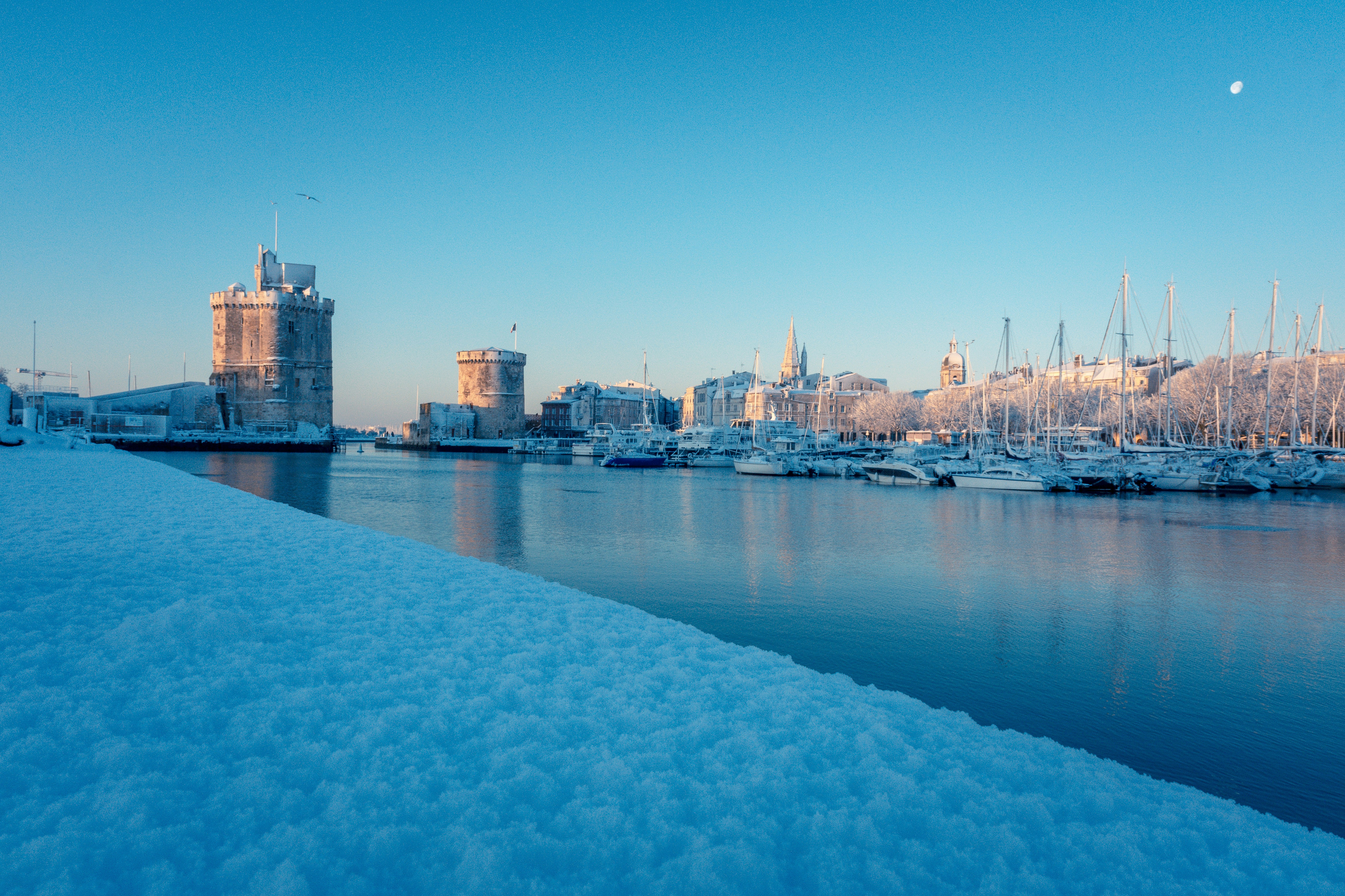 Snowy harbor with boats and buildings under clear sky