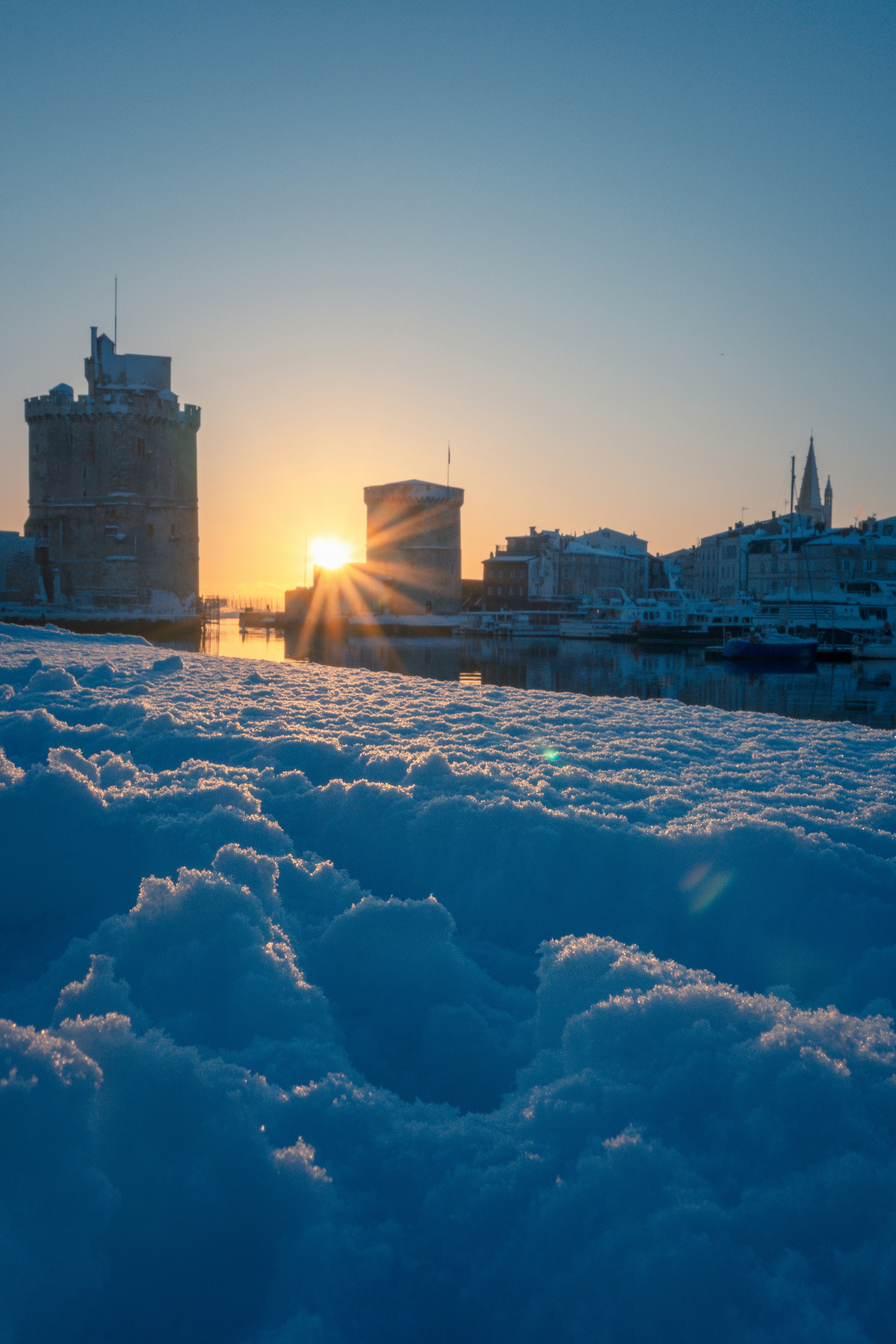 Snowy harbor with historic towers at sunrise.