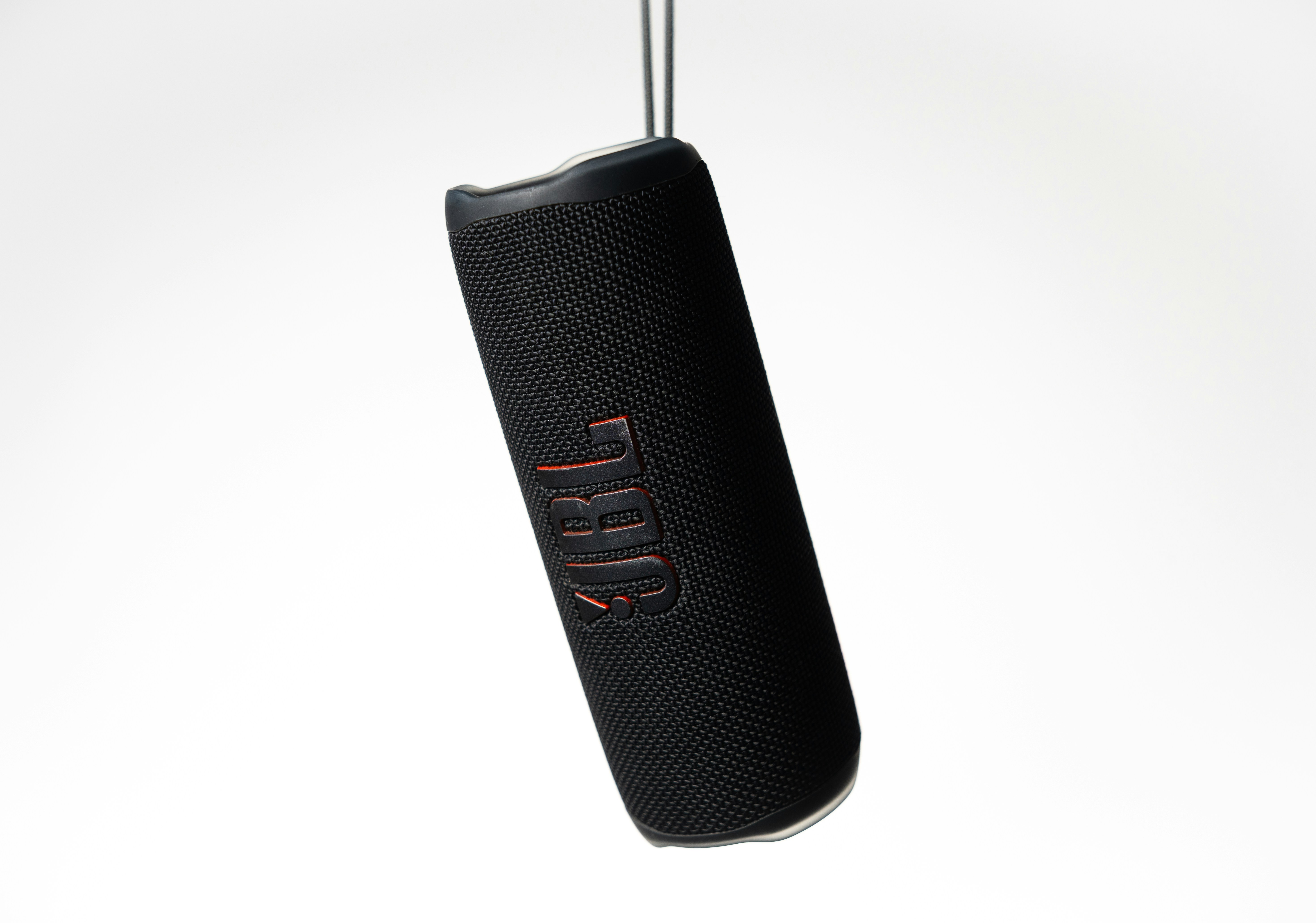 Altavoz portátil negro con logo naranja colgado