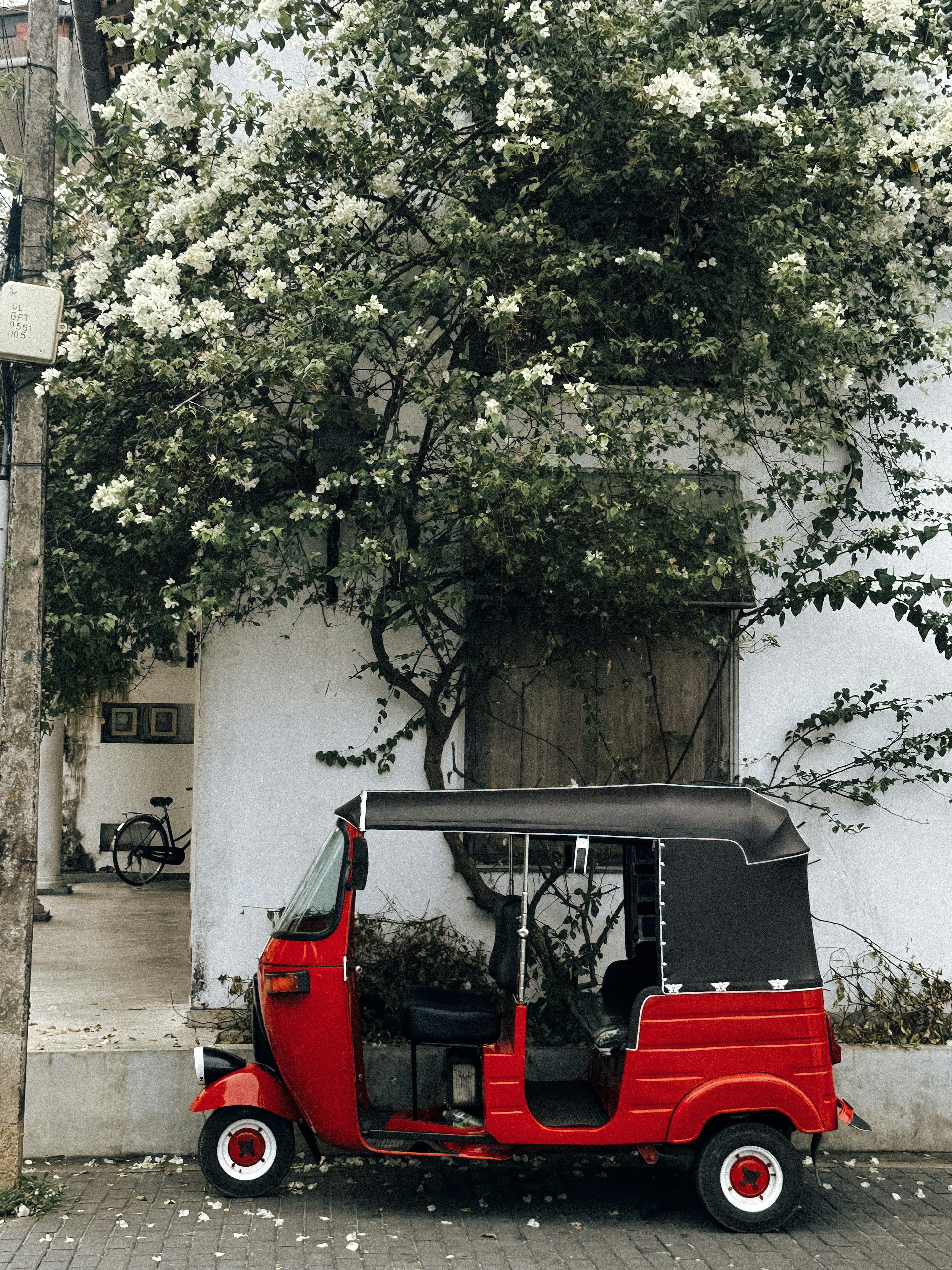 Red tuk-tuk parked beside a white wall with flowers.