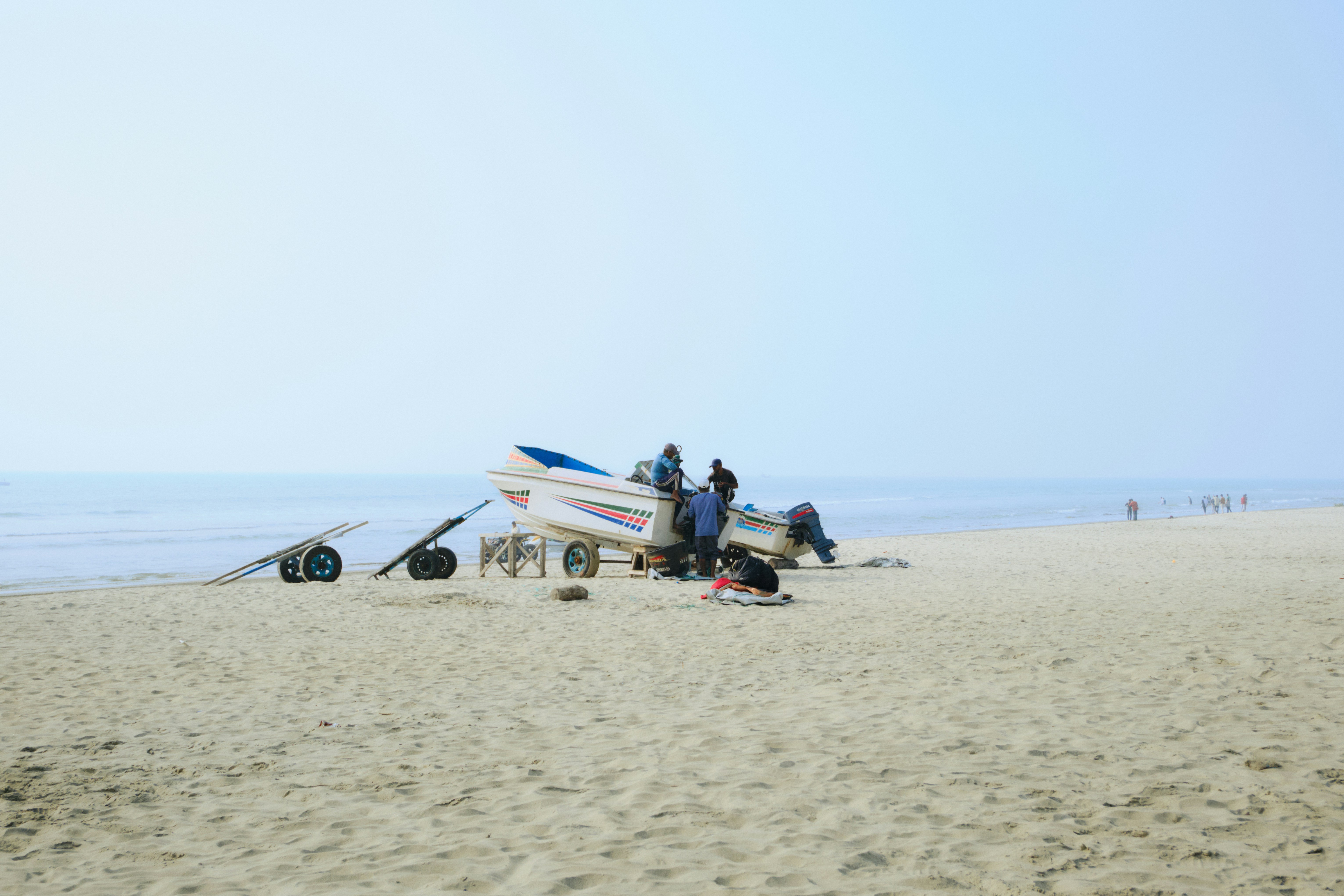 Pessoas se reuniam em torno de um barco em uma praia de areia.