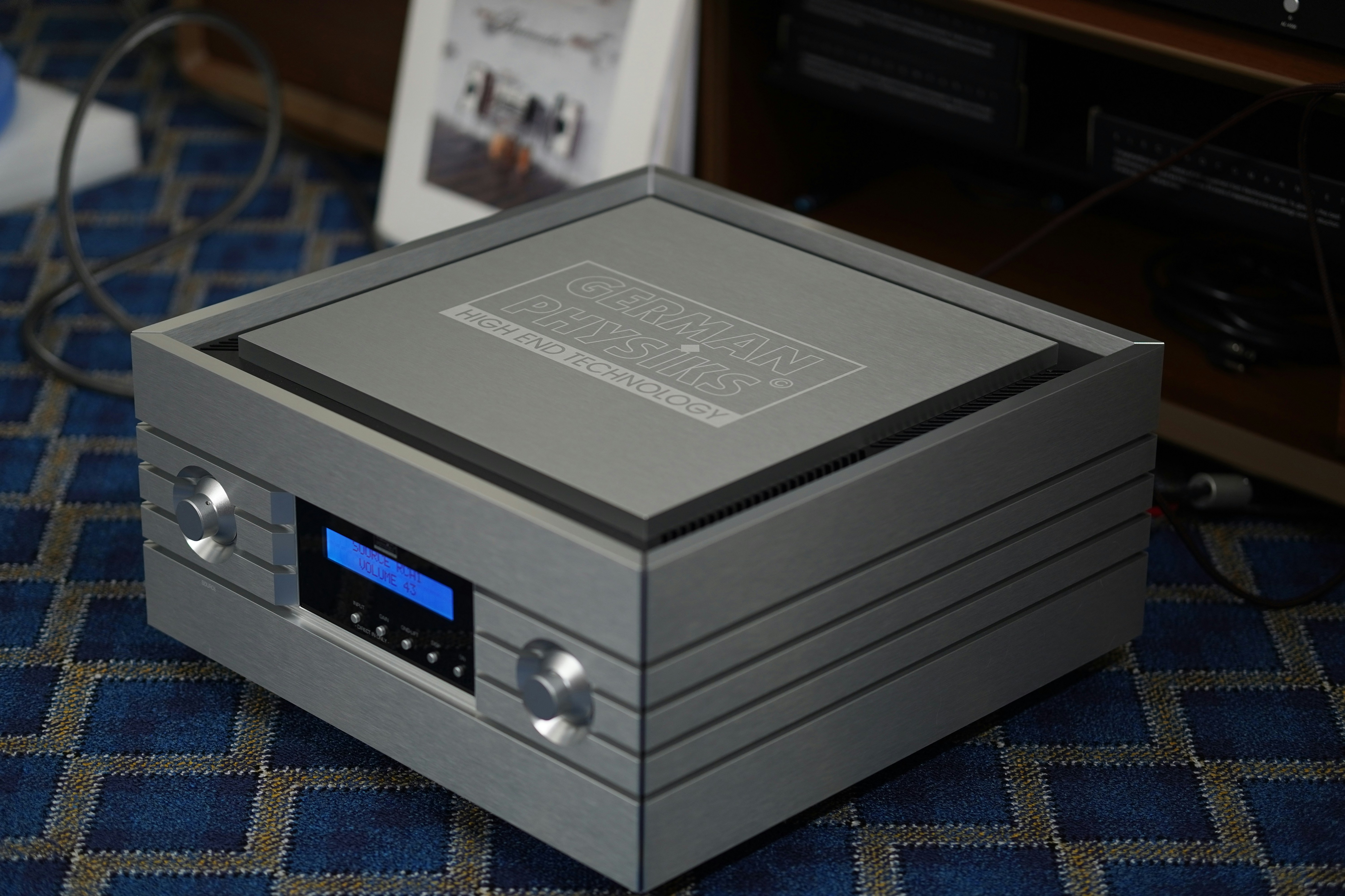 A modern silver audio amplifier with a blue display.