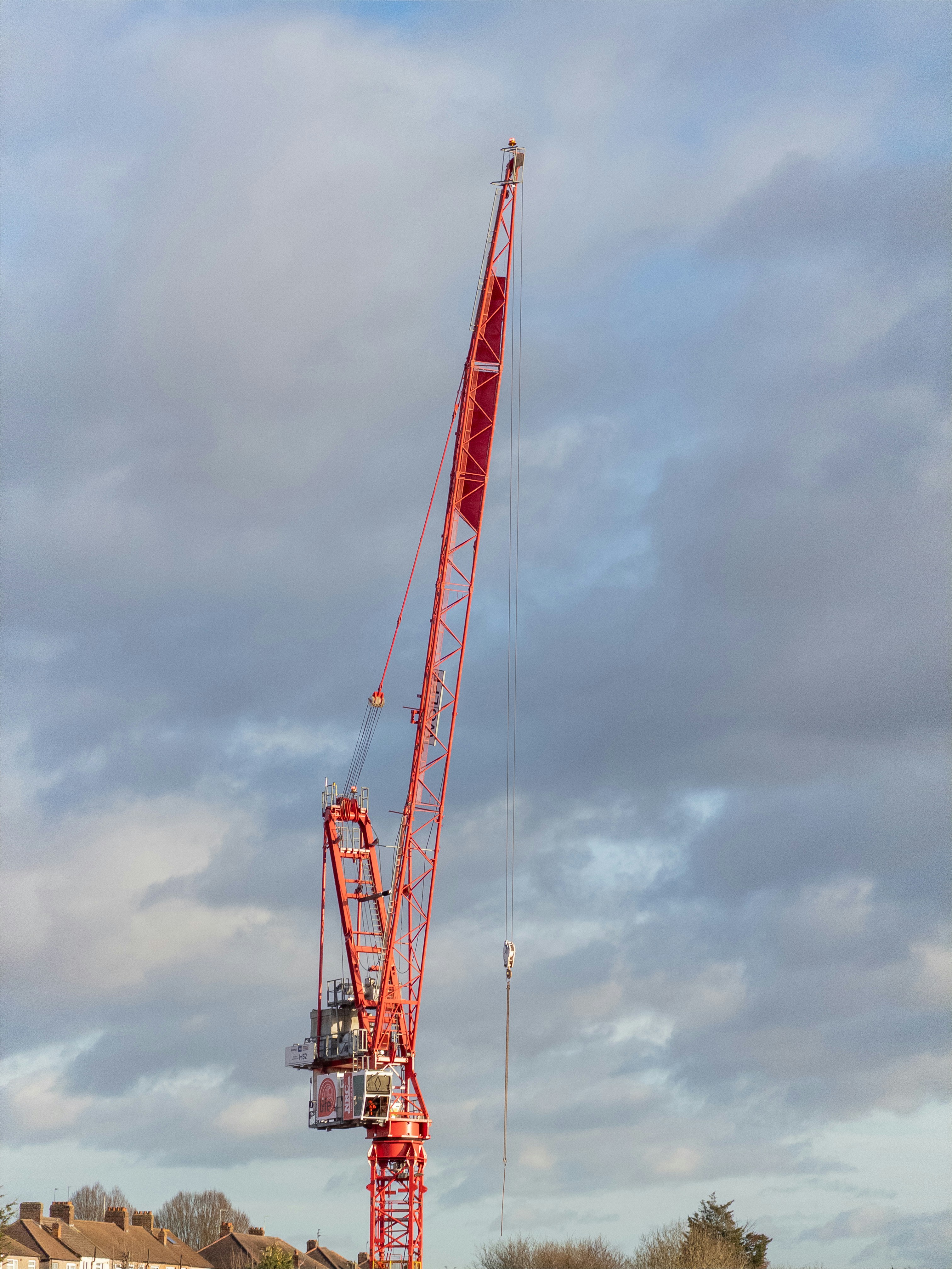 A tall red construction crane against a cloudy sky.