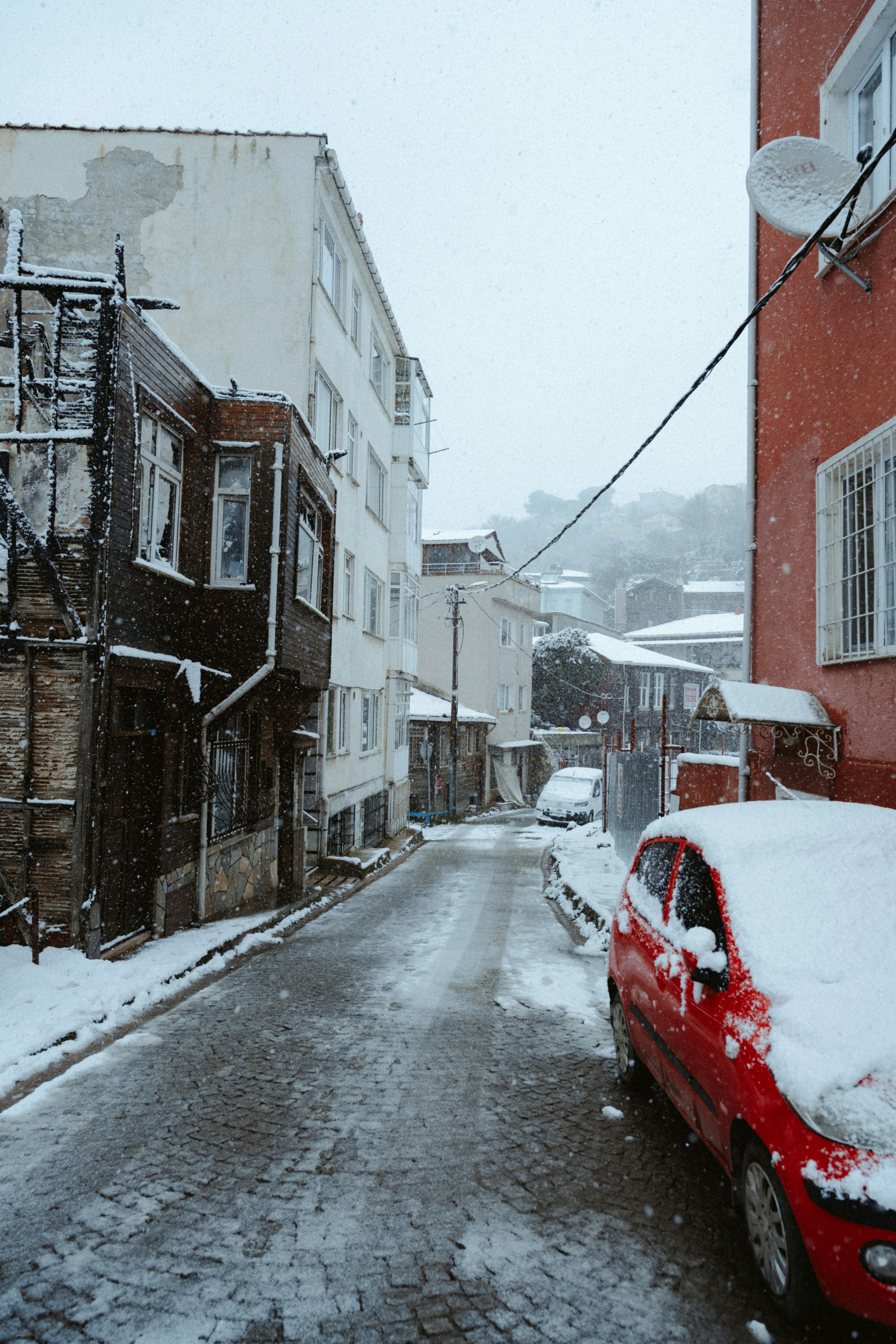 A street covered in snow with red car.