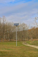 Solar panel stands in a grassy field near trees.