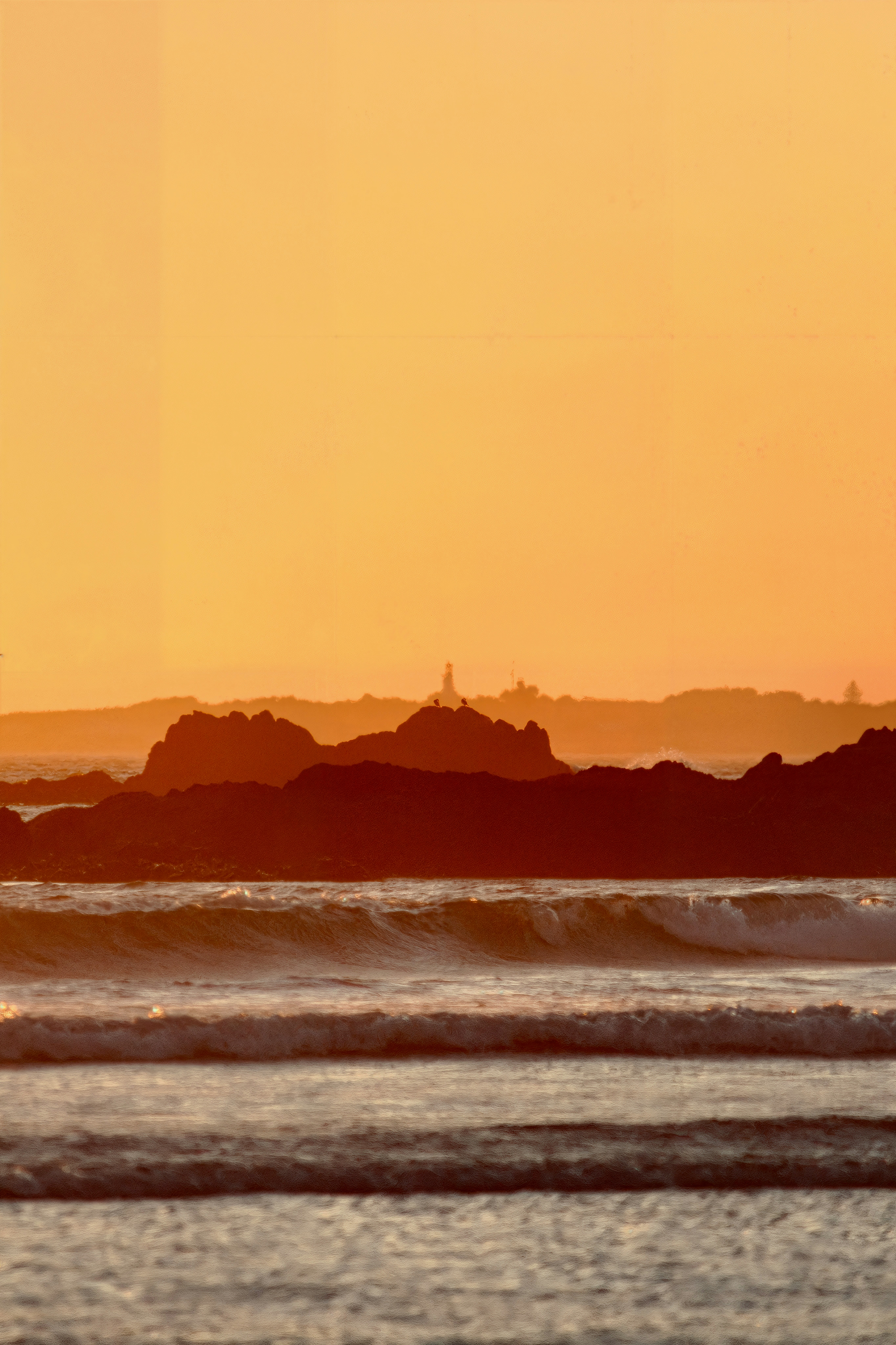 Waves crash on a rocky shore at sunset.
