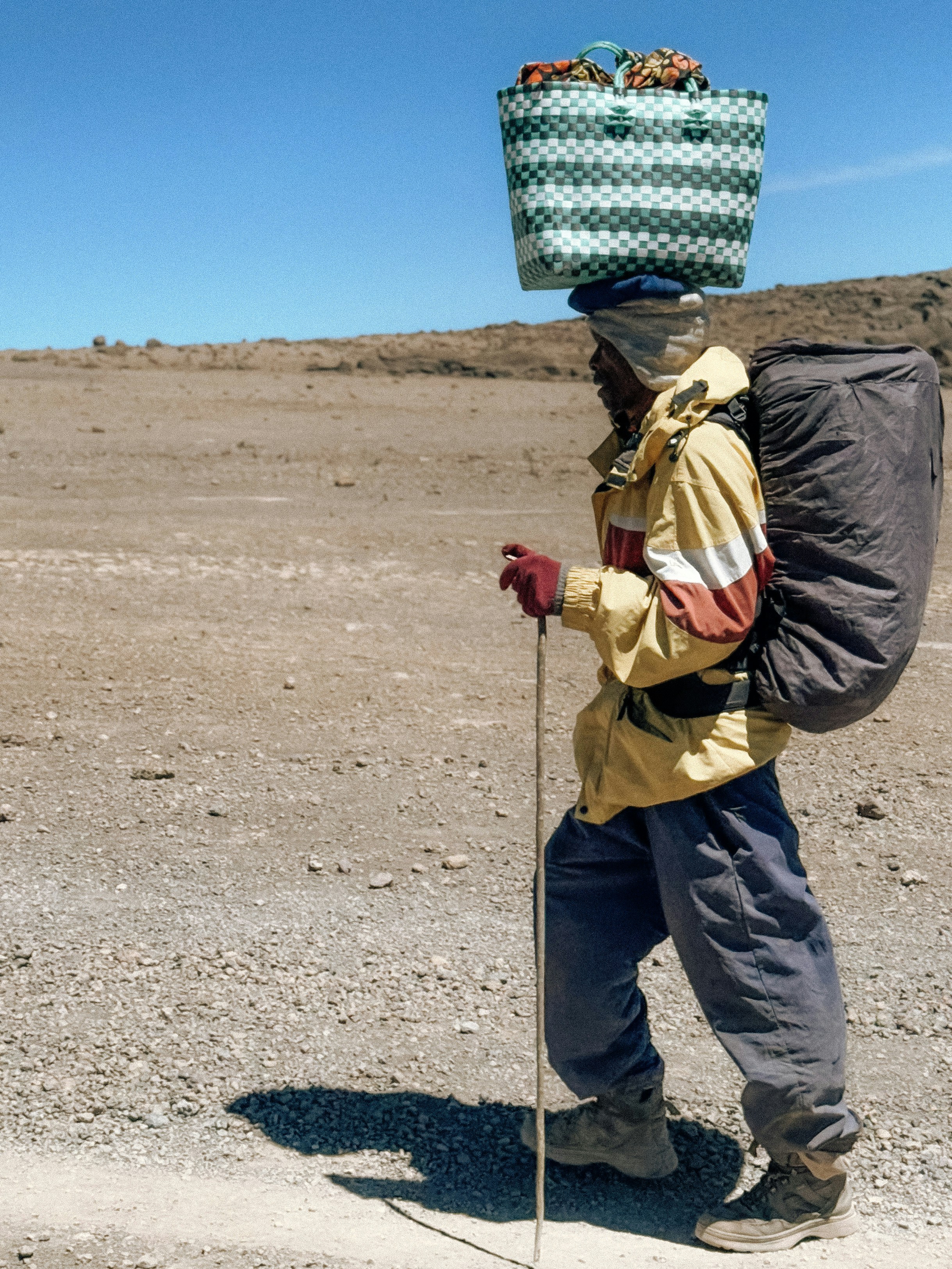 Man carrying basket and backpack on a dirt path.