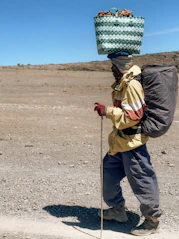 Man carrying basket and backpack on a dirt path.