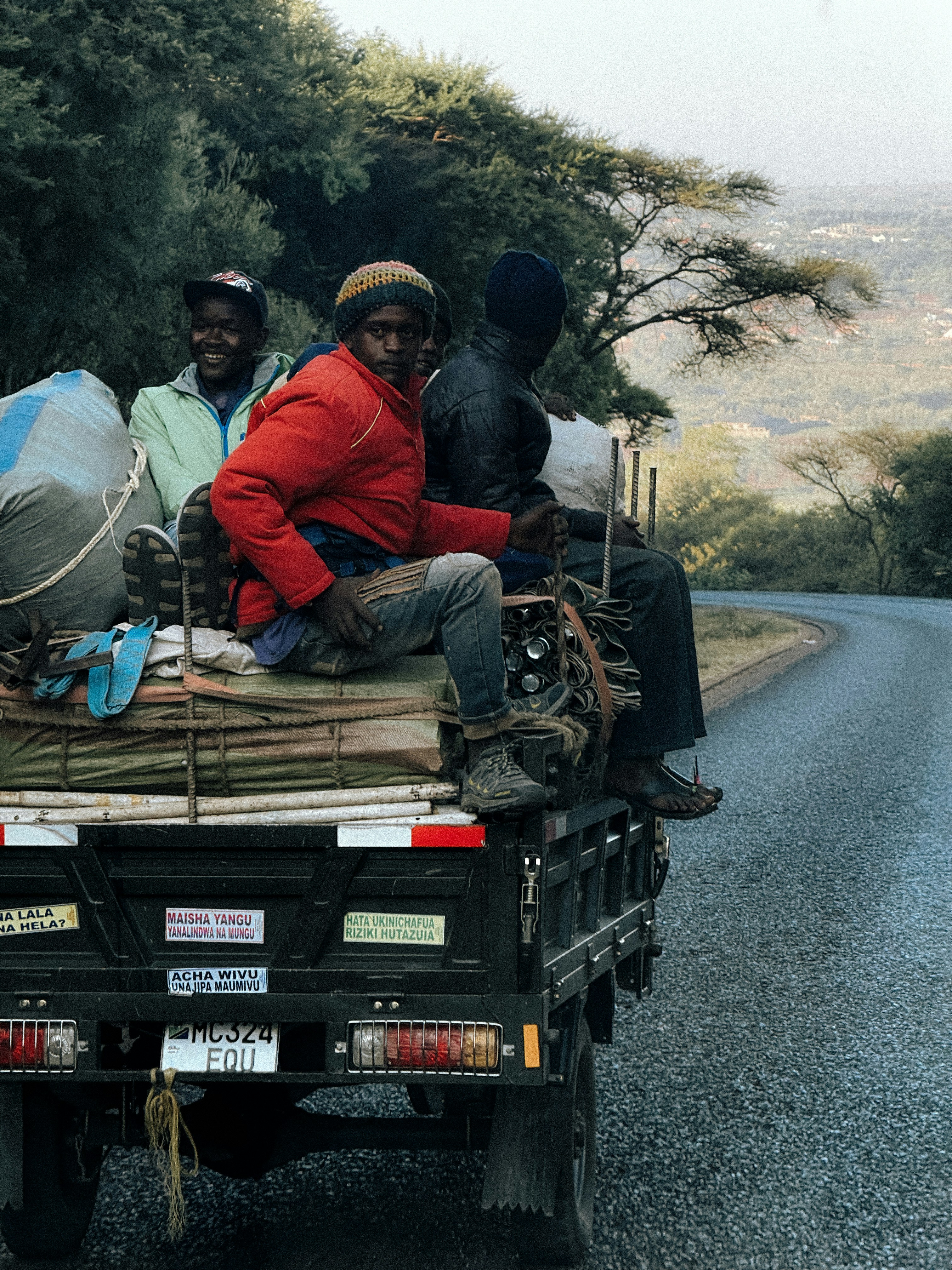 Three people ride in the back of a truck.