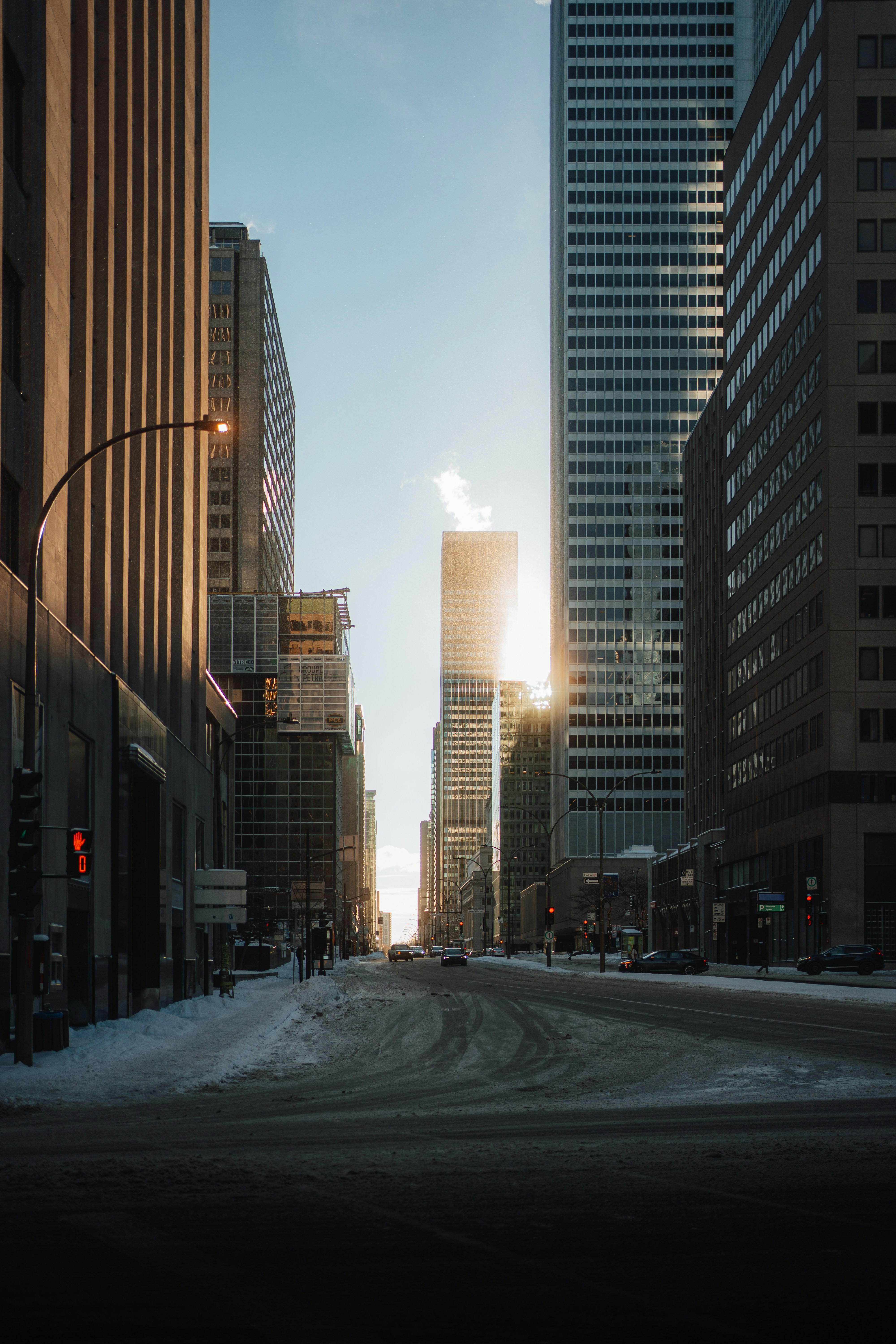 Sunlight shines between tall buildings on a snowy street.