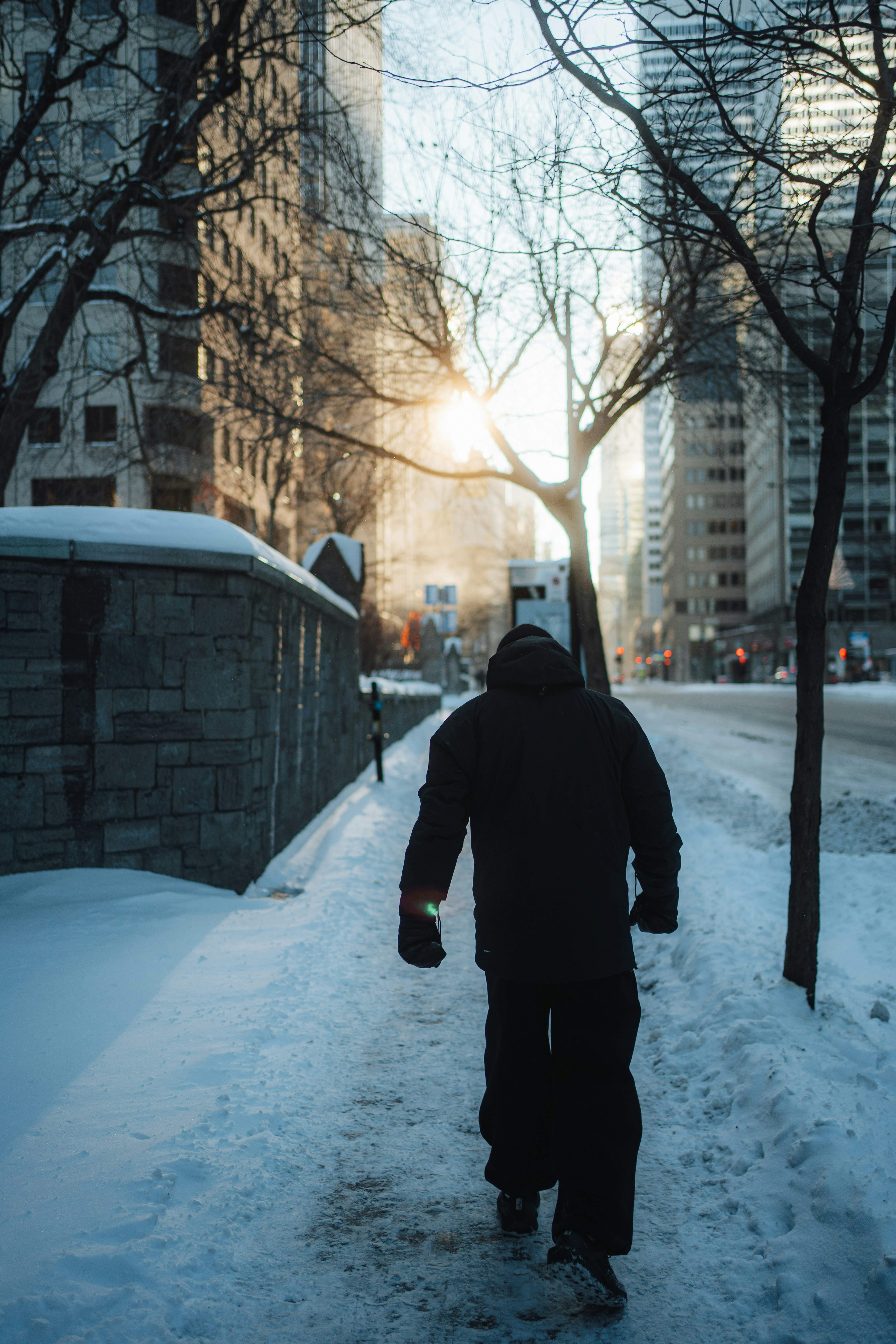 A person walks down a snowy city sidewalk at sunset.