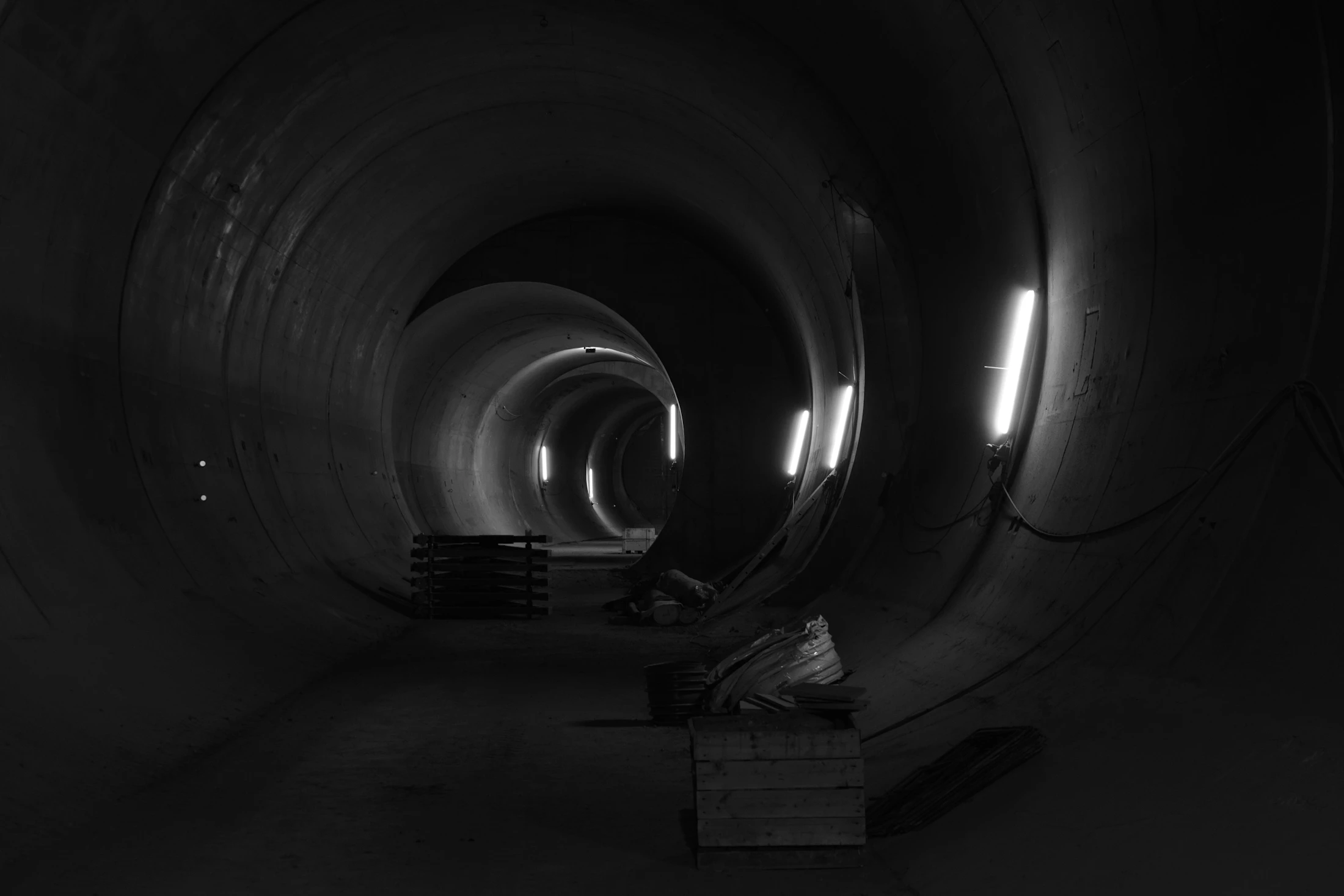 Tunnel cylindrique en construction éclairé par des rampes techniques.
