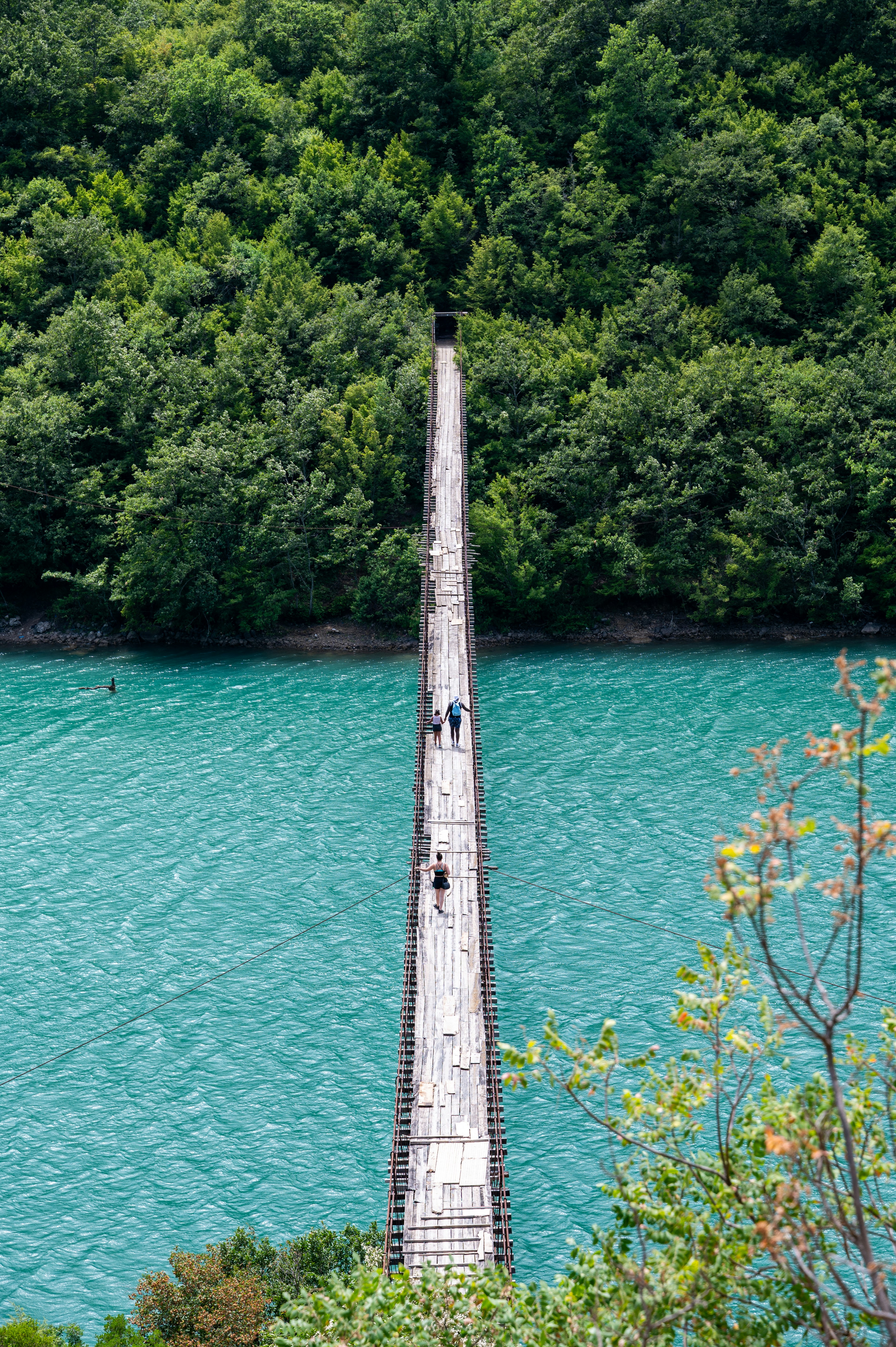 People walk across a long suspension bridge over water.