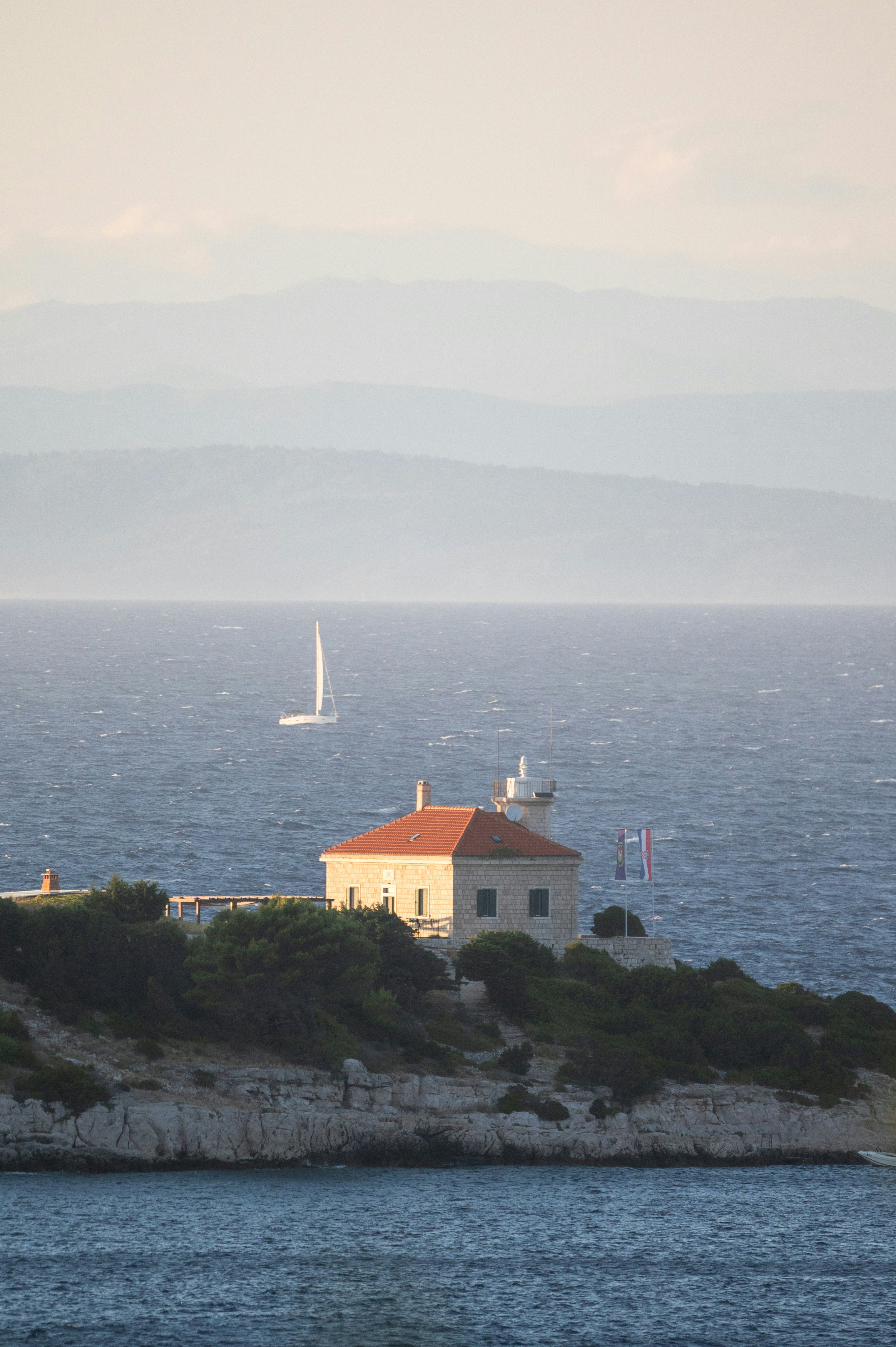 Lighthouse on island with sailboat in distance.
