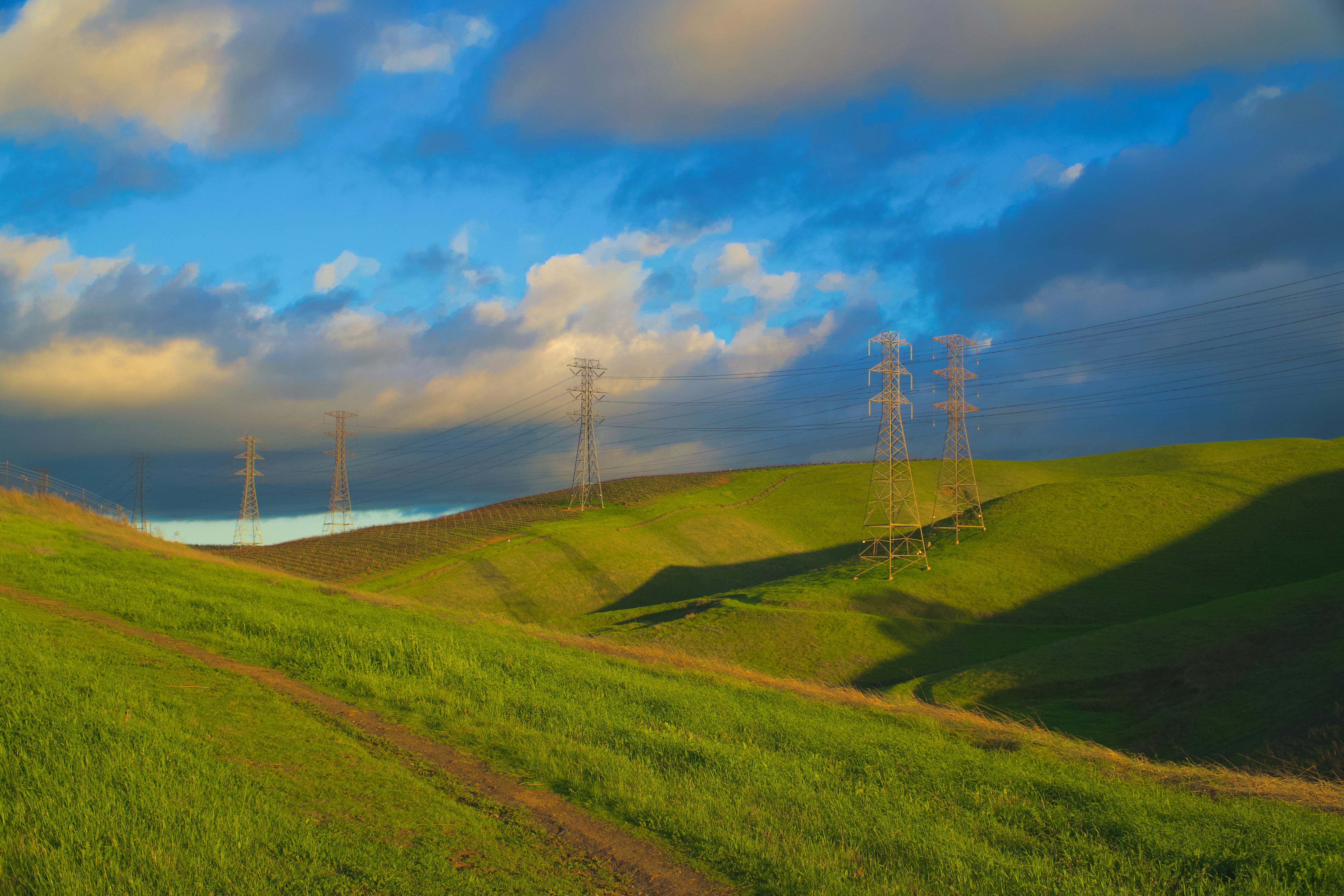 Rolling green hills with power lines under clouds
