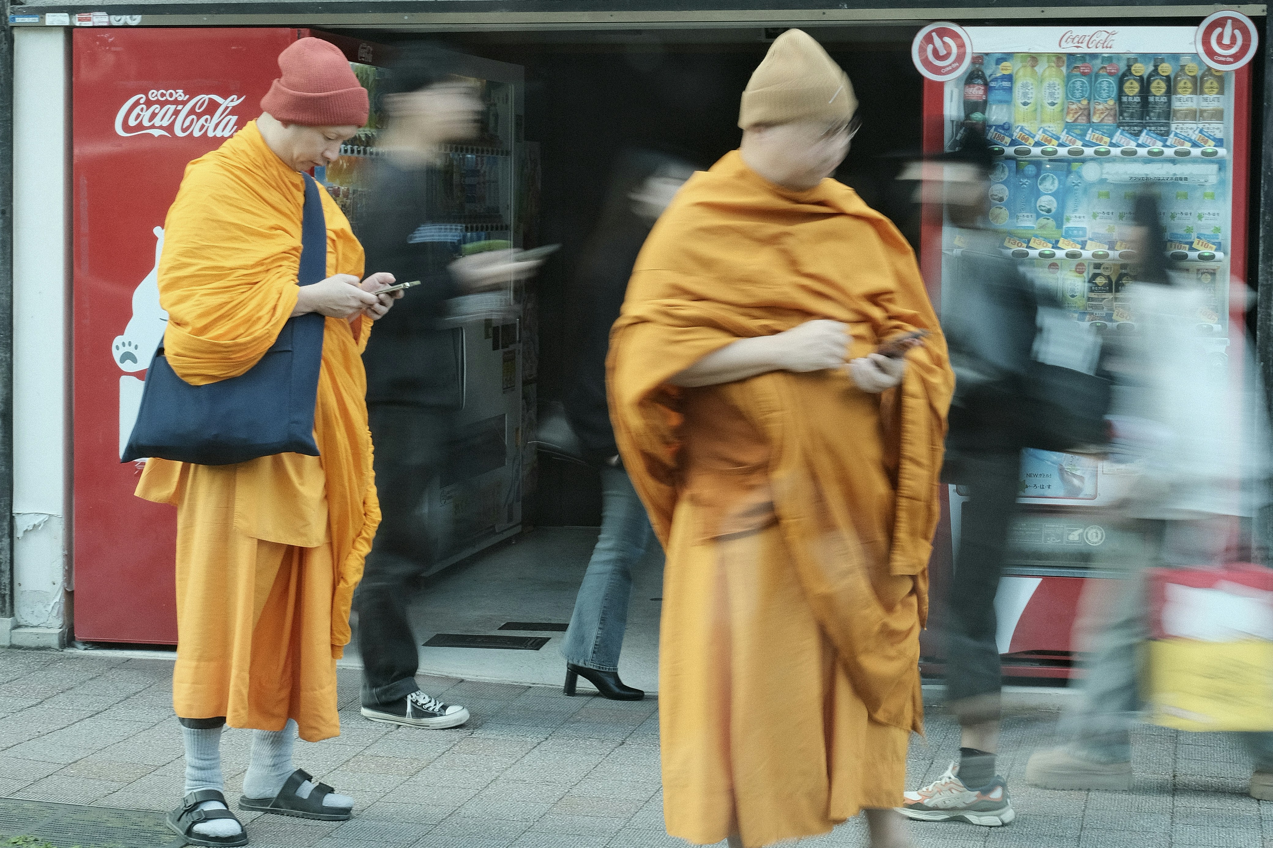 Two monks in orange robes stand near a vending machine.