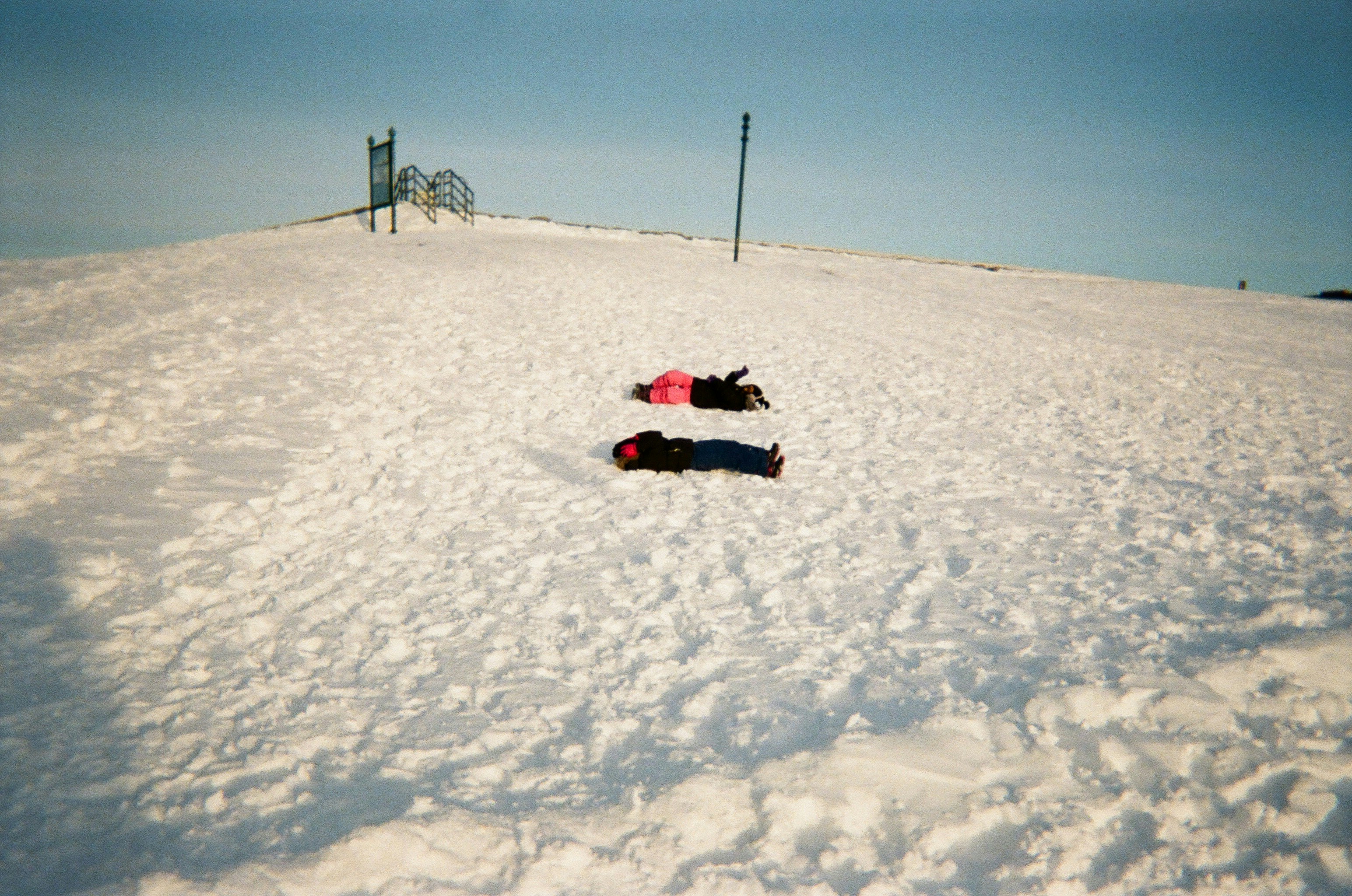 Two people making snow angels on a sunny day.