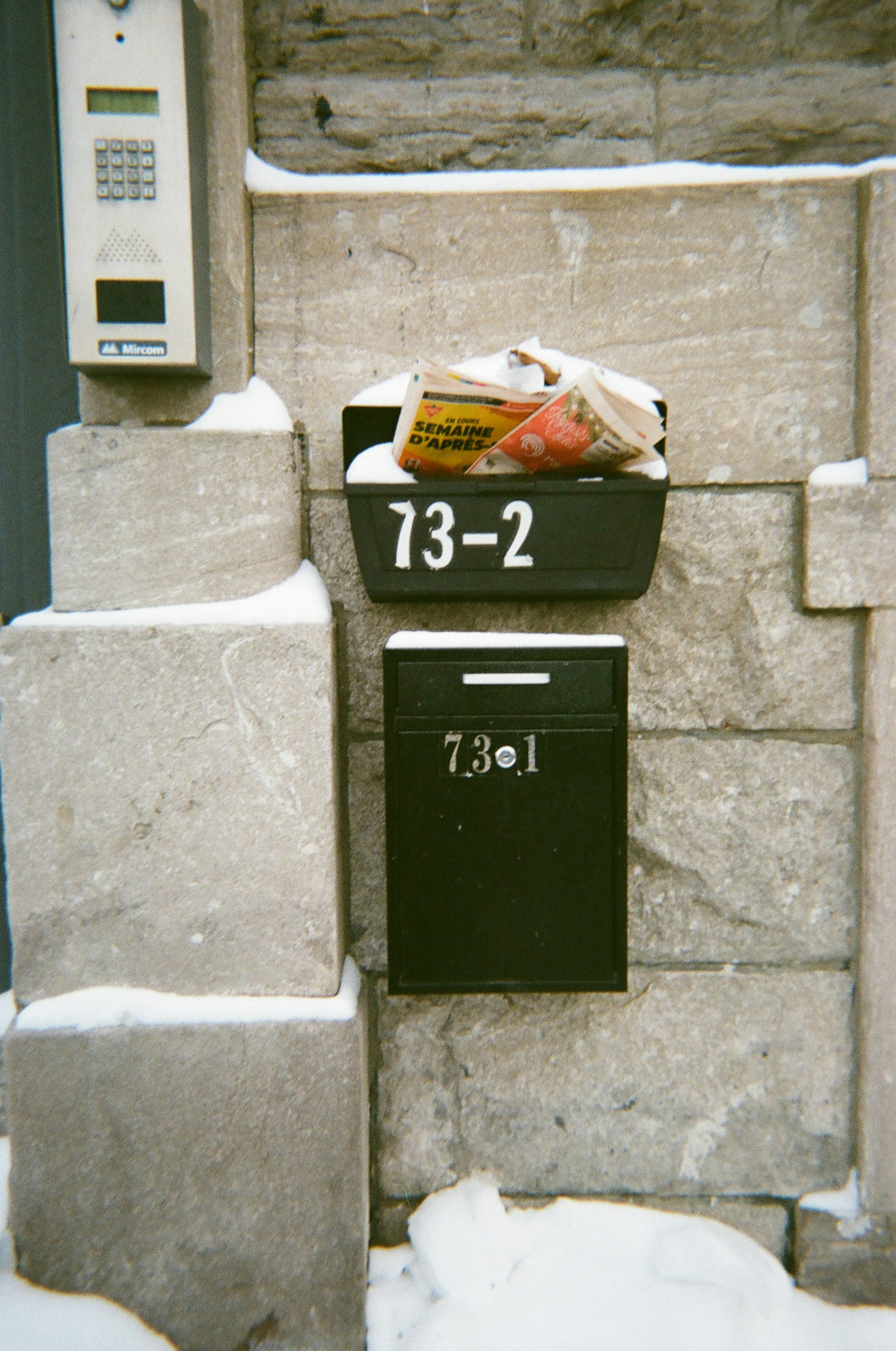 Two mailboxes on a stone wall with snow.