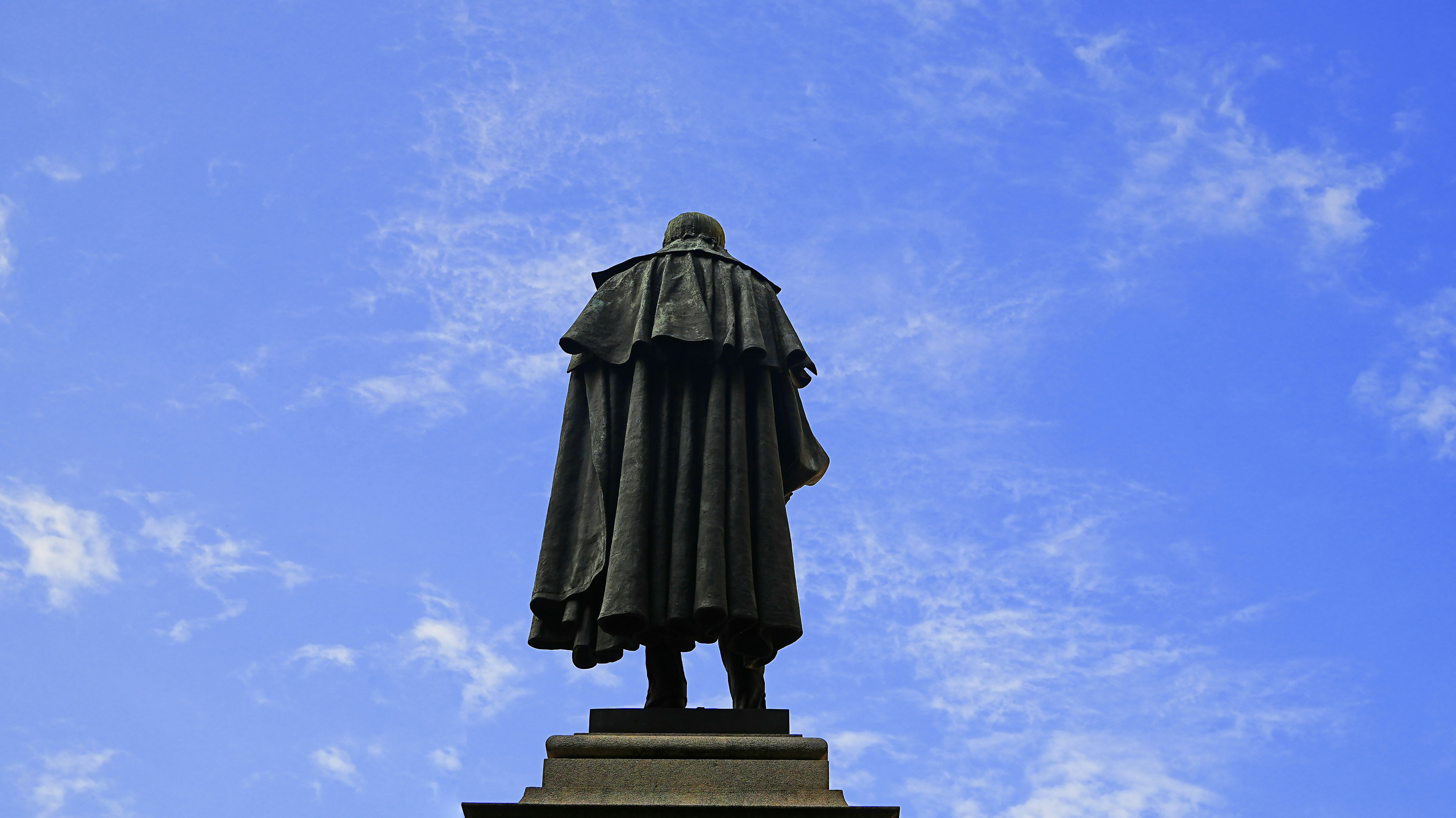 Statue viewed from behind against a blue sky.