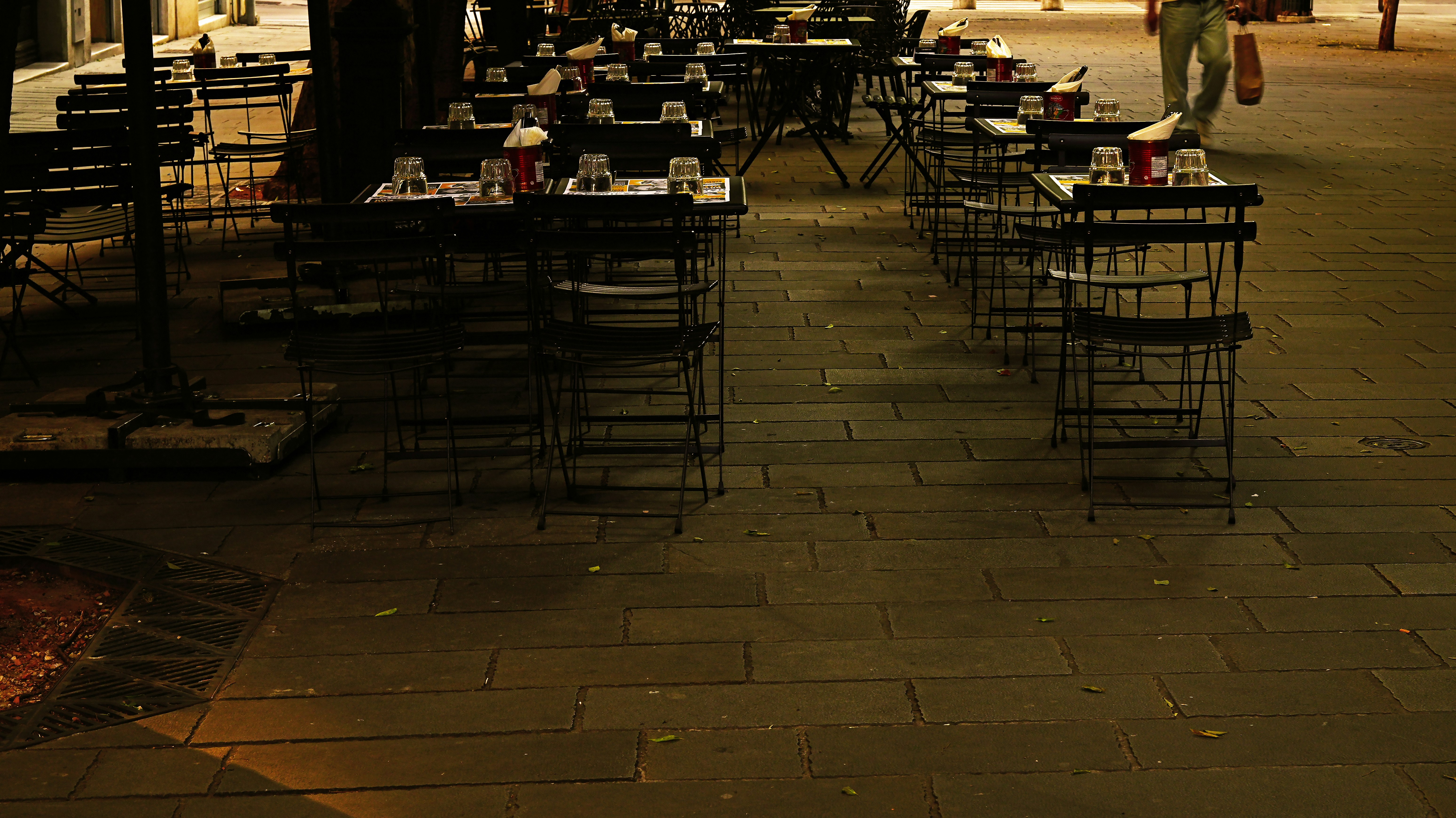 Empty outdoor cafe tables at dusk on a sidewalk.