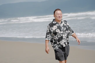 An elderly man walks on a sandy beach.