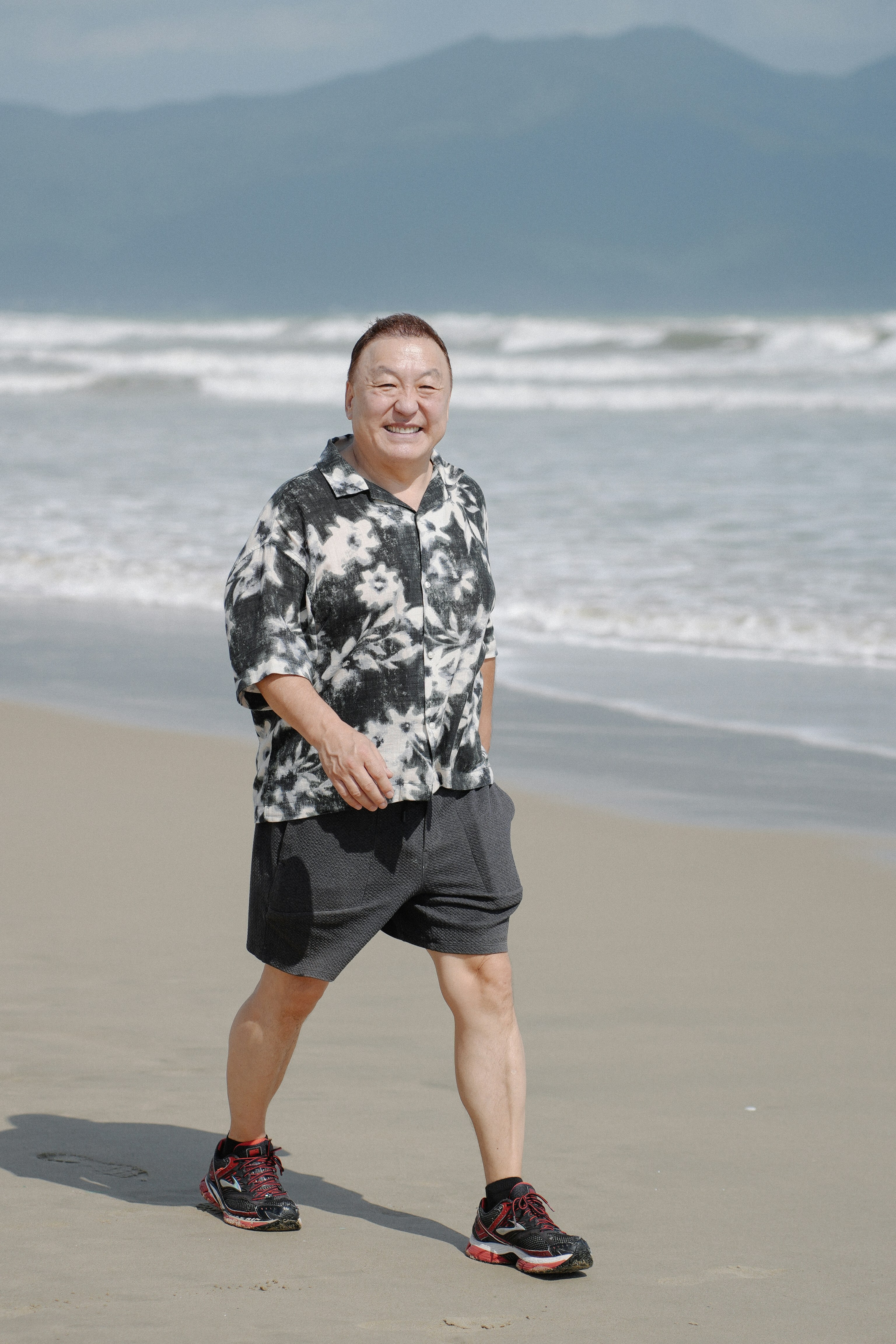 Smiling man walks on a sandy beach near ocean.