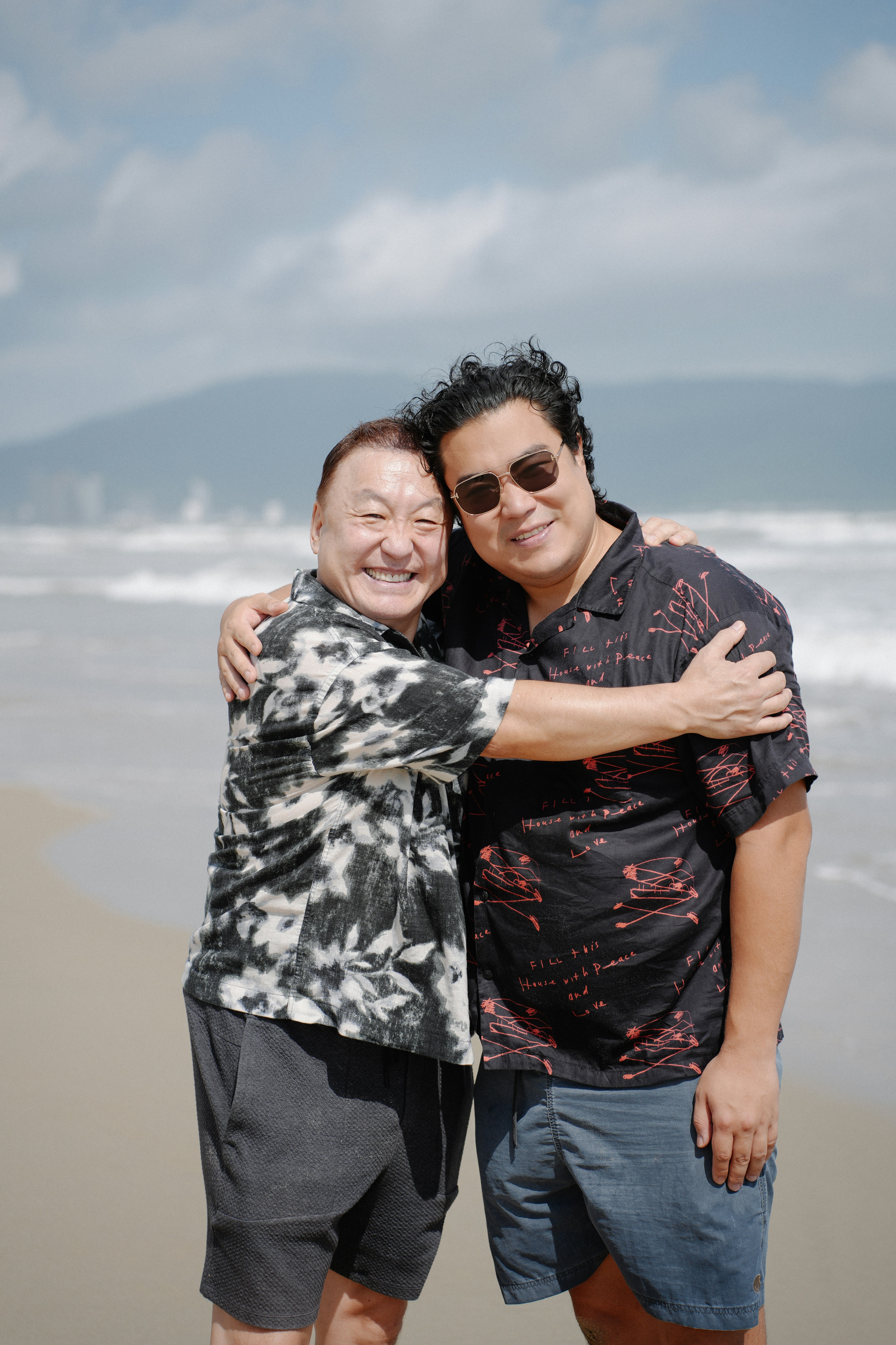 Two men hugging on a beach with ocean background