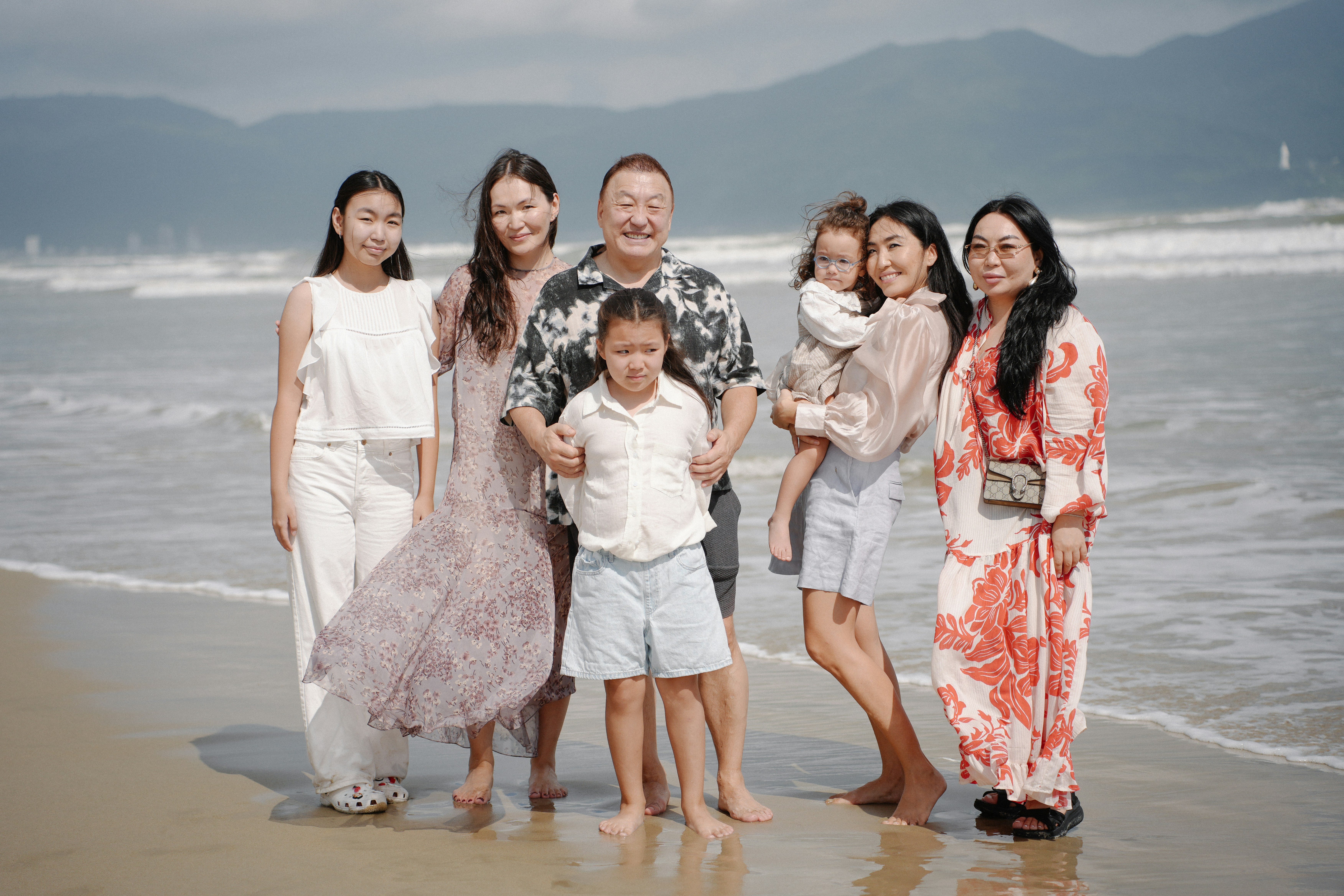 Familie, die an einem Strand posiert, mit den Meereswellen hinter sich.