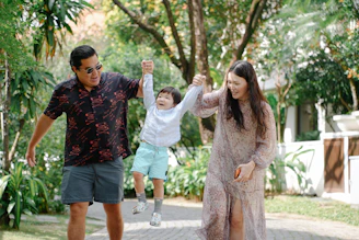Parents swing their happy son between them outdoors