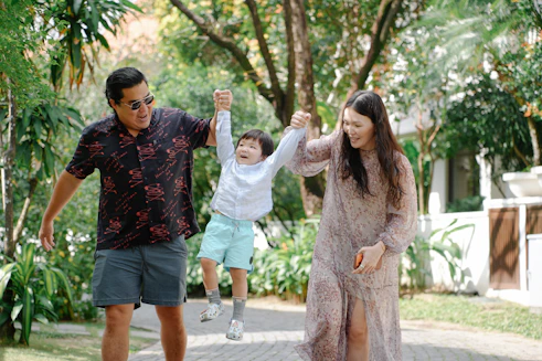 Parents swing their happy son between them outdoors