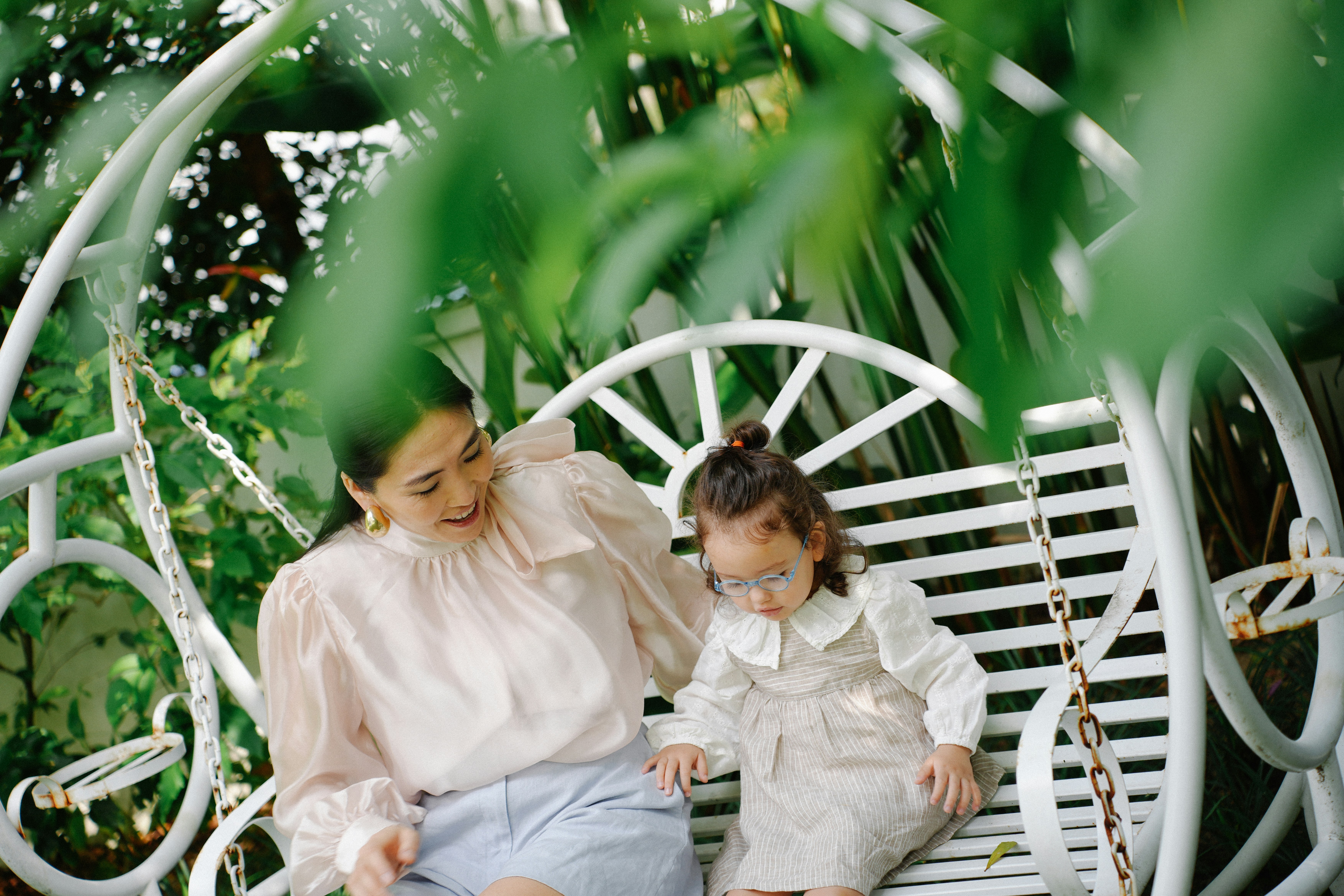 Mother and daughter sitting on a white swing.