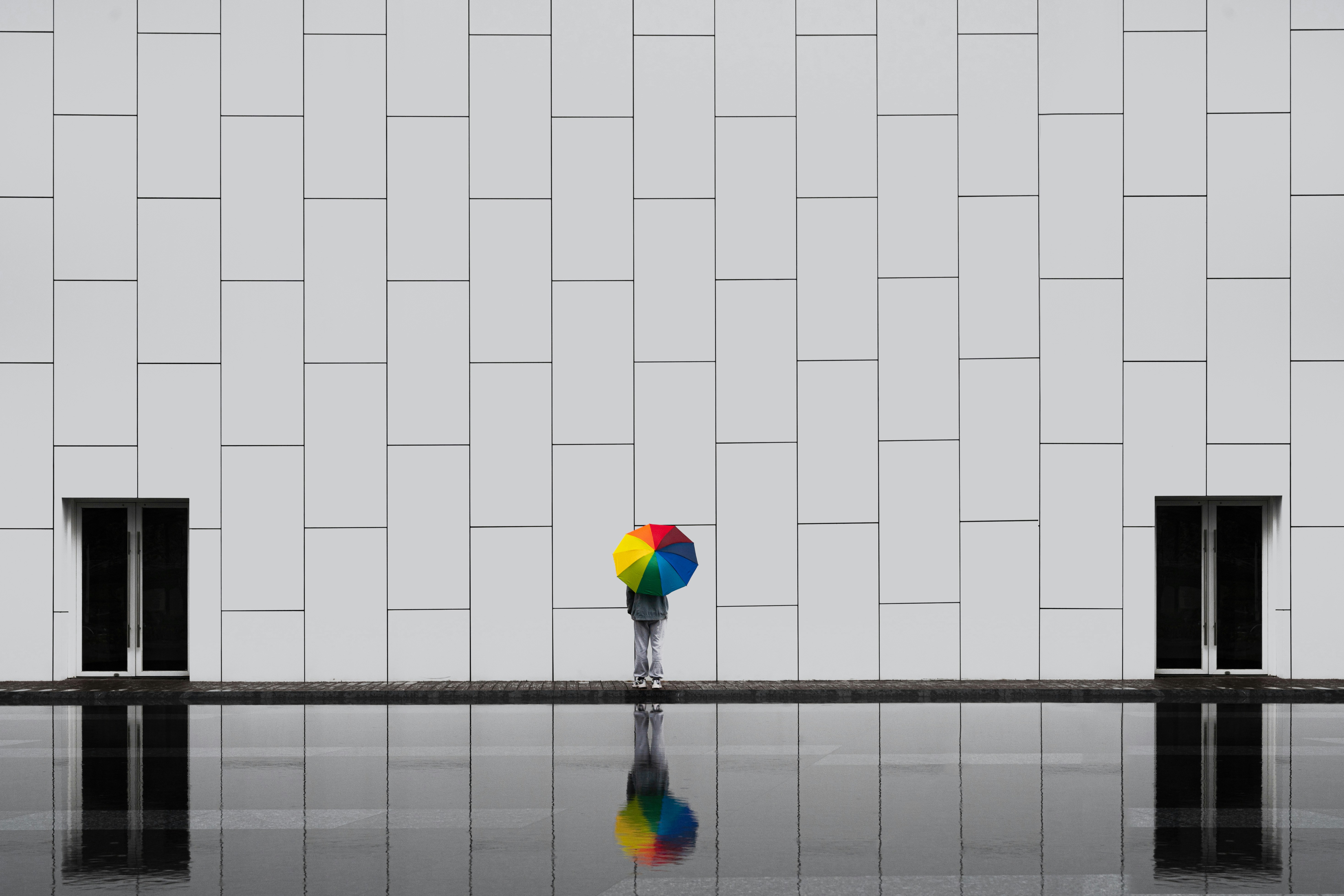 Person with rainbow umbrella by reflective pool